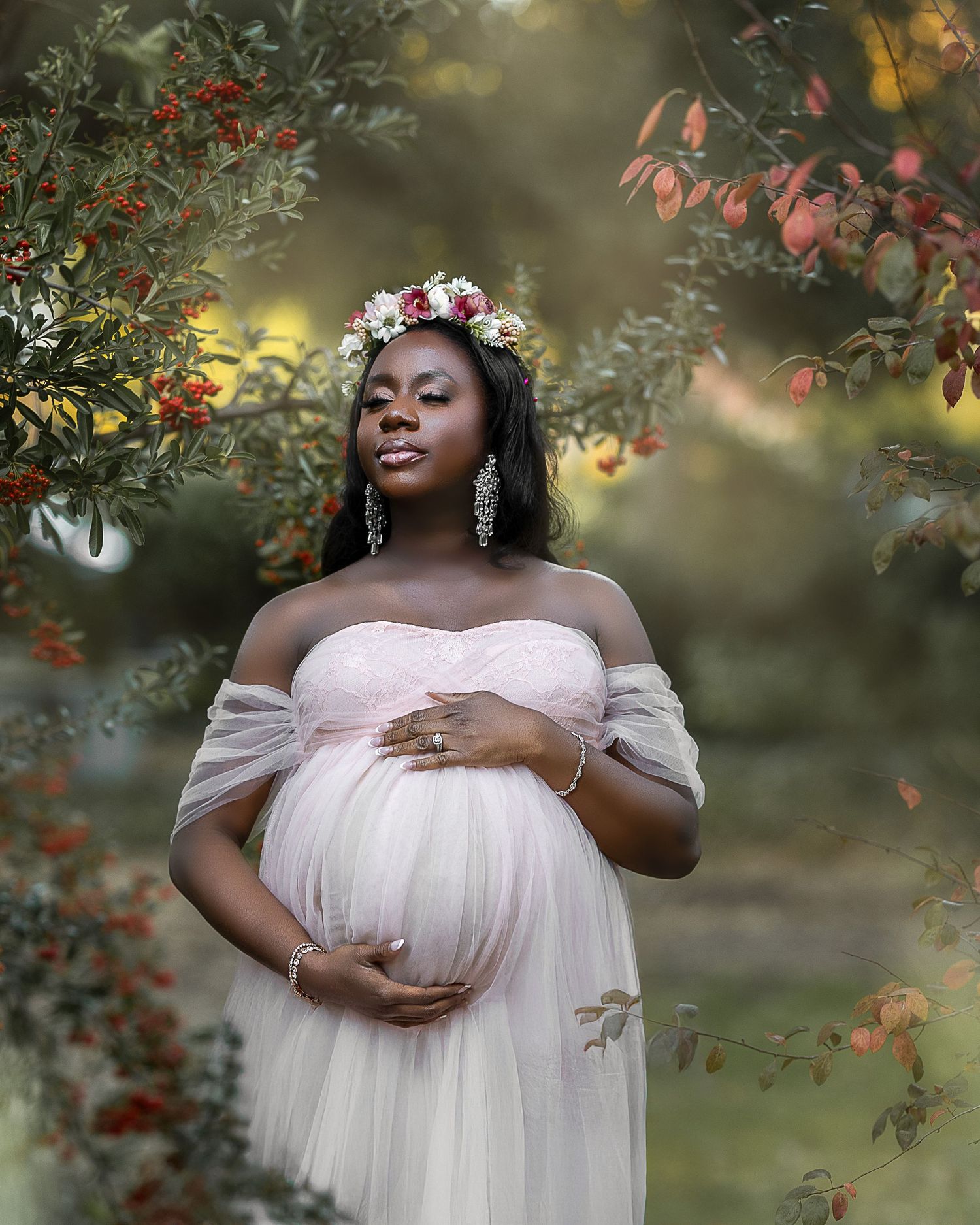 A maternity photoshoot in a garden setting with soft lighting and ethereal white tulle fabric creating a dreamy atmosphere.