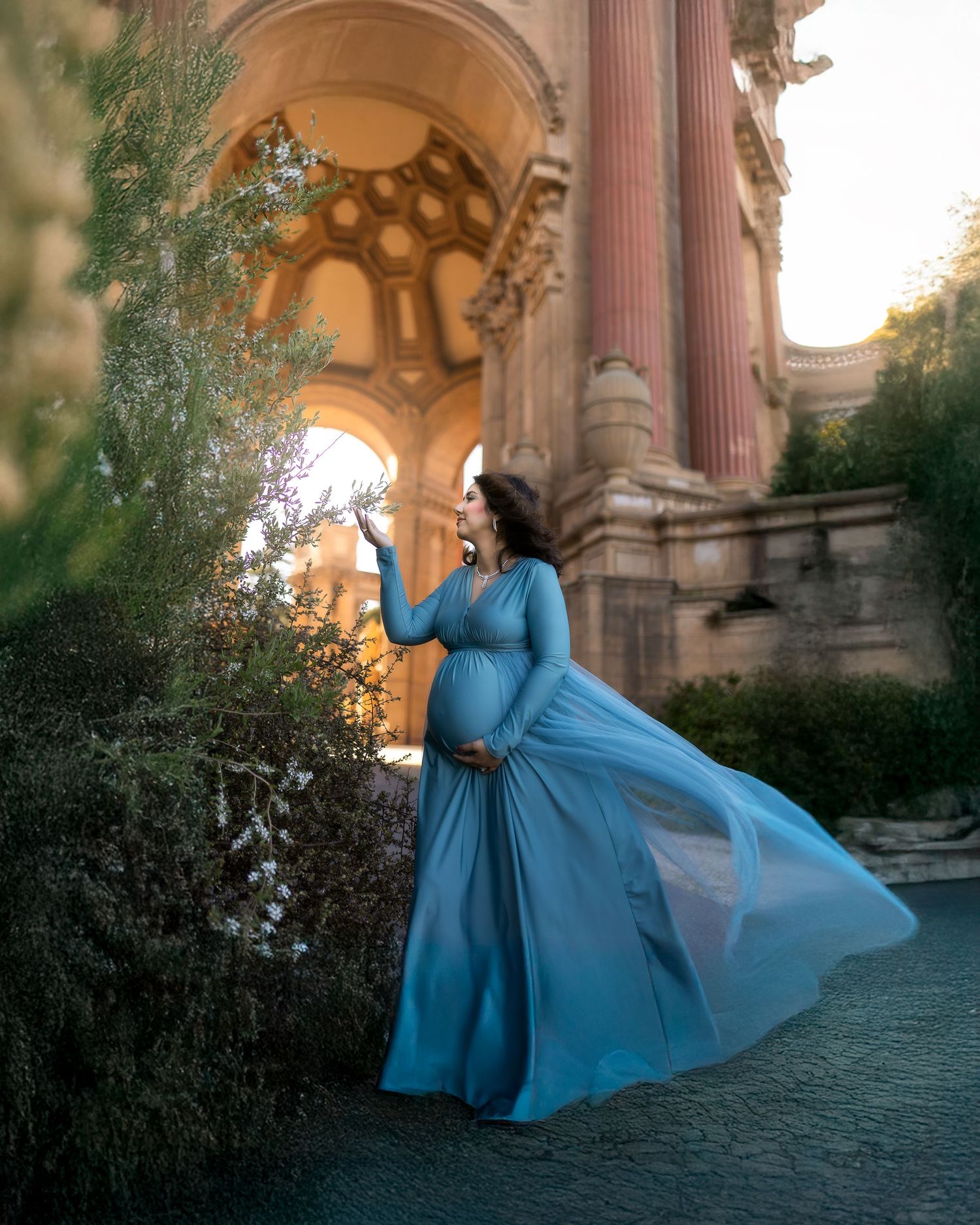 A flowing turquoise gown billows elegantly against the backdrop of classical architecture at sunset.