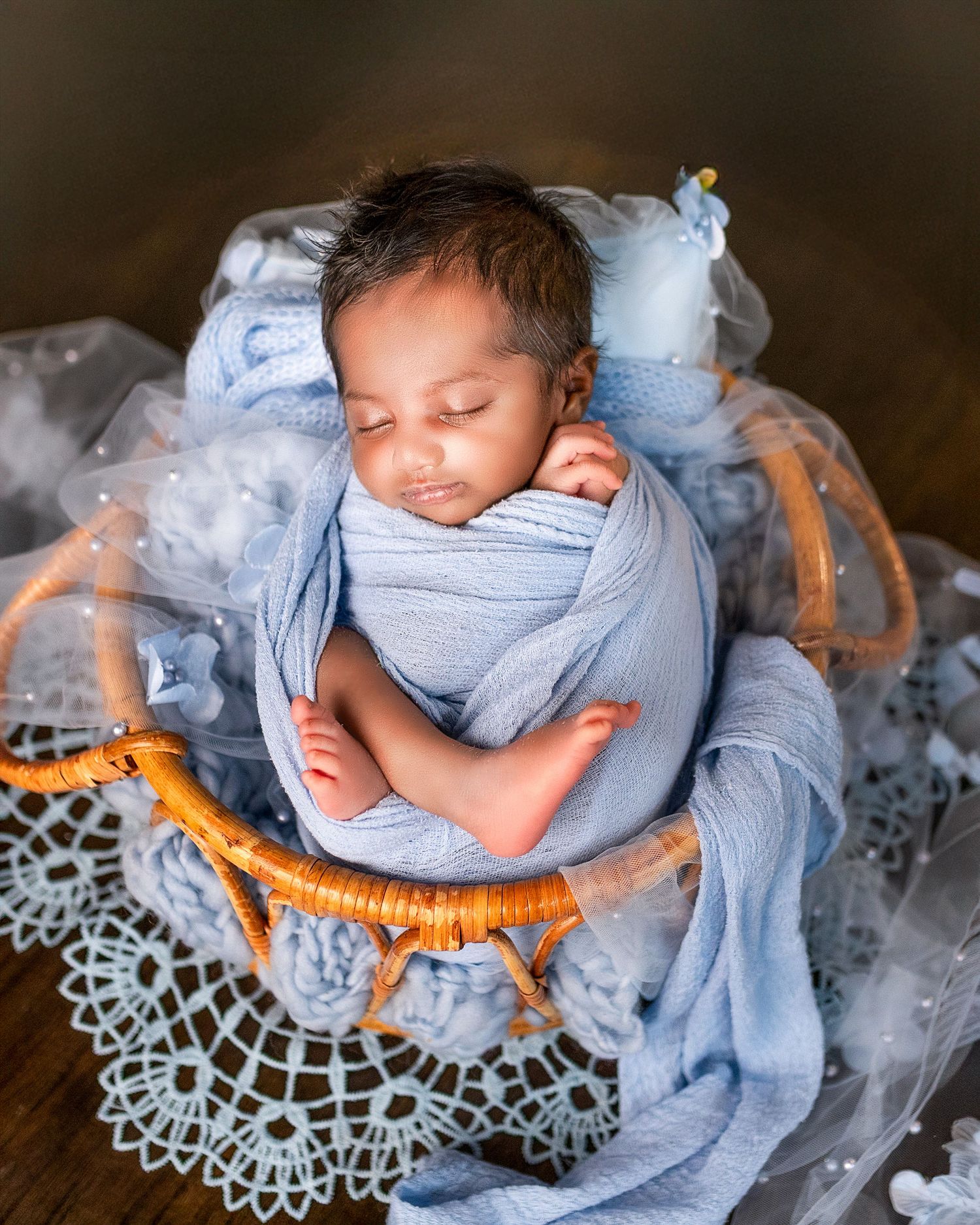 Newborn photography series showing sleeping baby wrapped in light blue fabric on delicate lace doily.