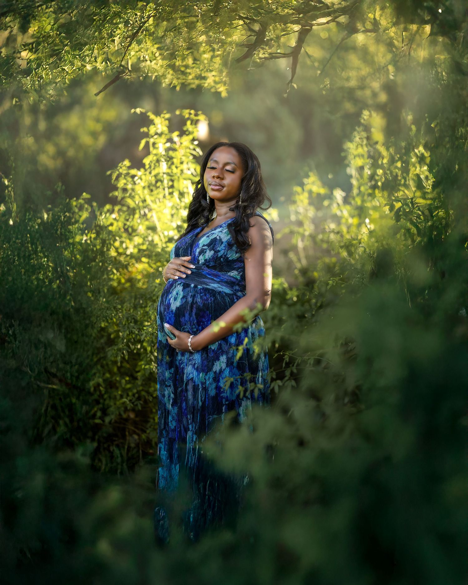 A figure in a flowing blue dress stands gracefully against a sunlit natural backdrop with green foliage.