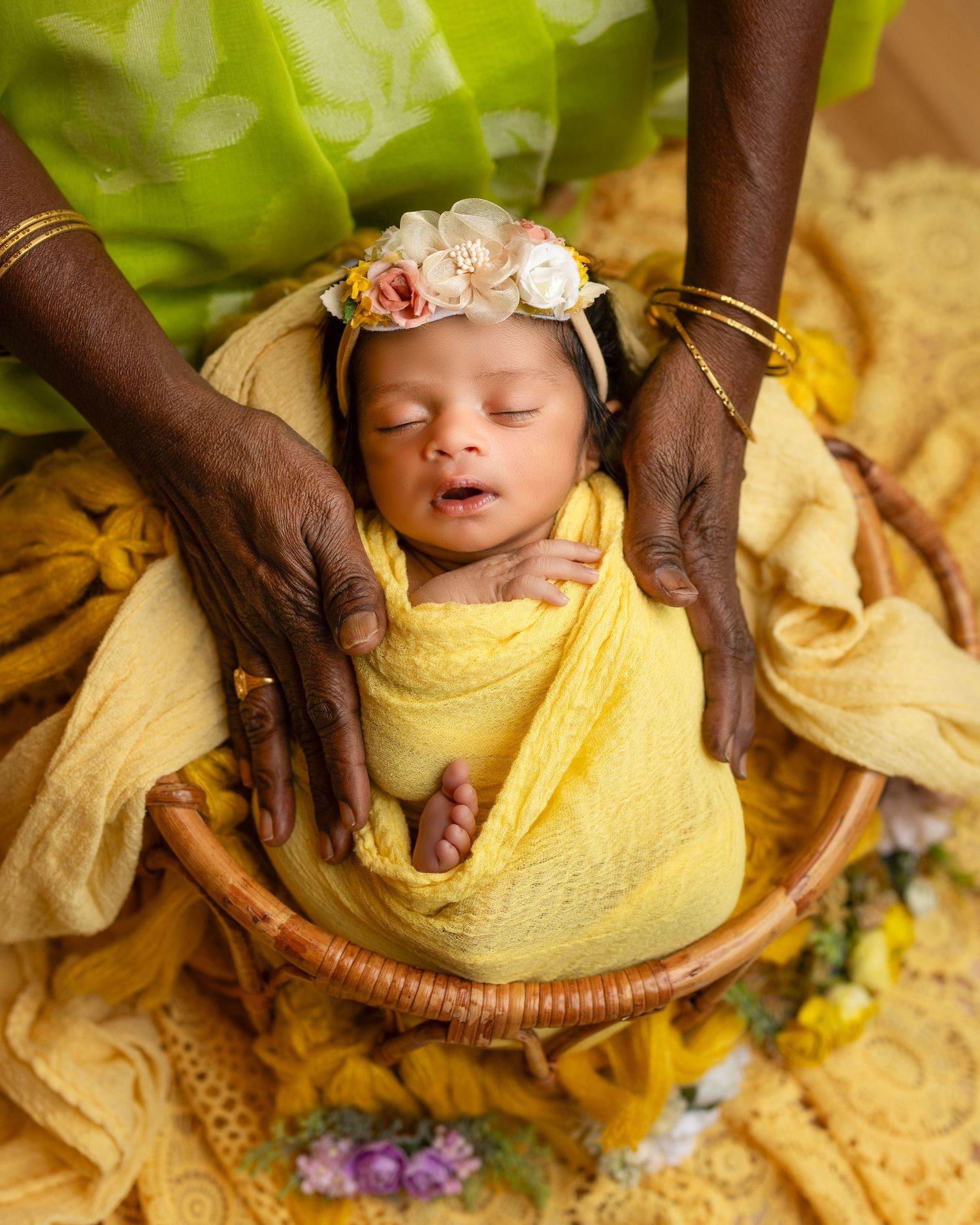 Newborn wrapped in soft yellow fabric nestled in wooden bowl with autumn leaves and floral accents.