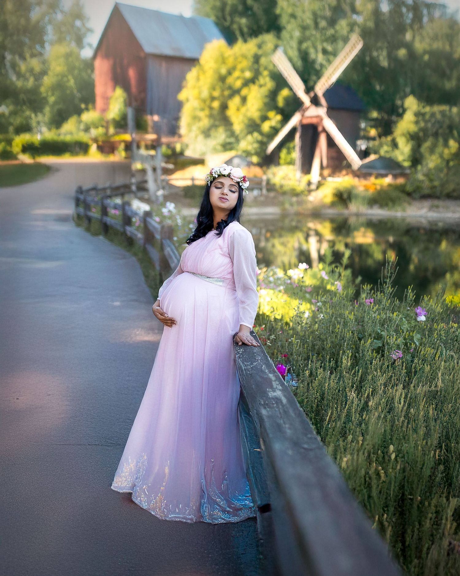 A dreamy maternity photo session captured in a rustic outdoor setting with tall grass and a barn in the background.