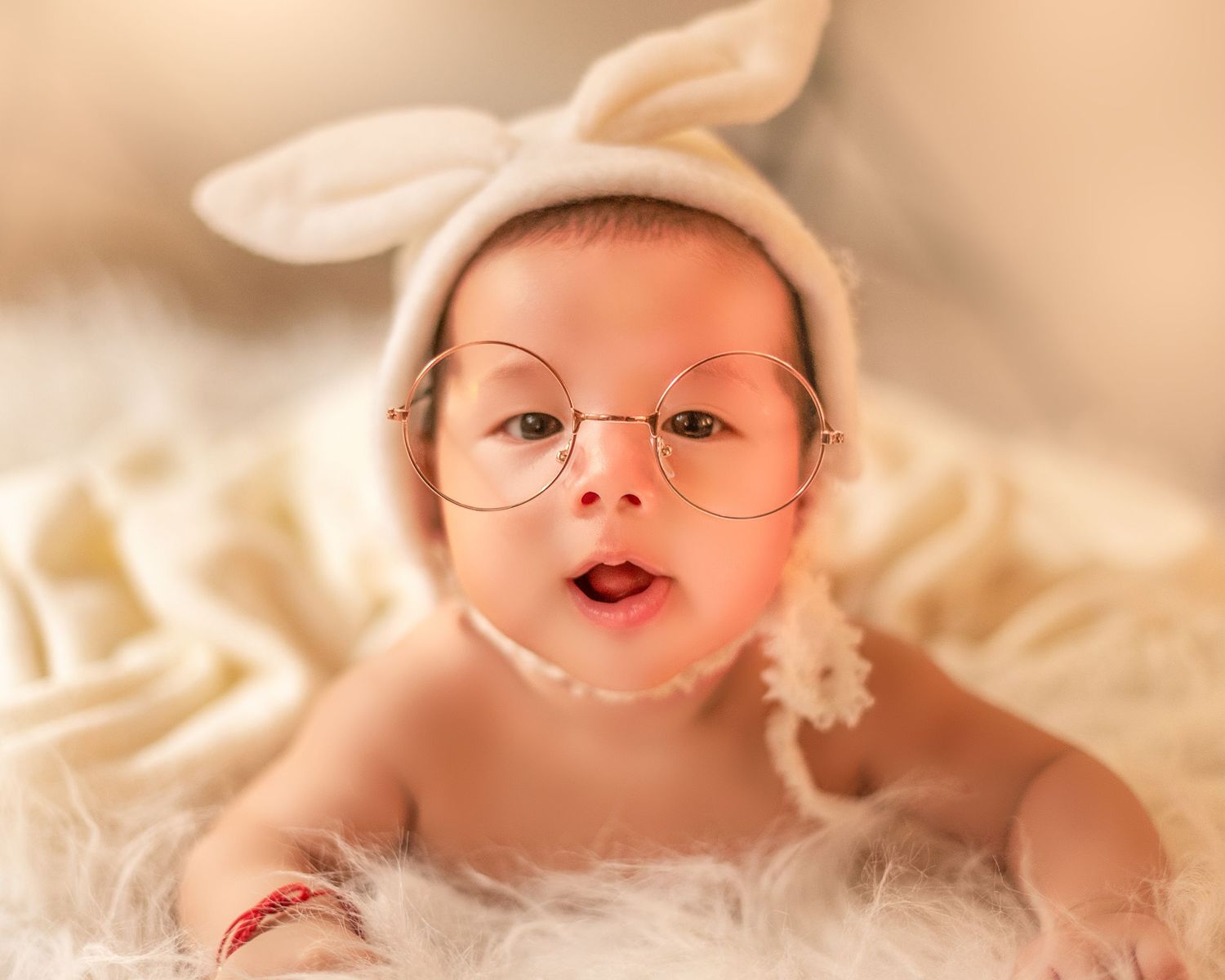 A baby lies on soft white fabric with a joyful smile and rosy cheeks.