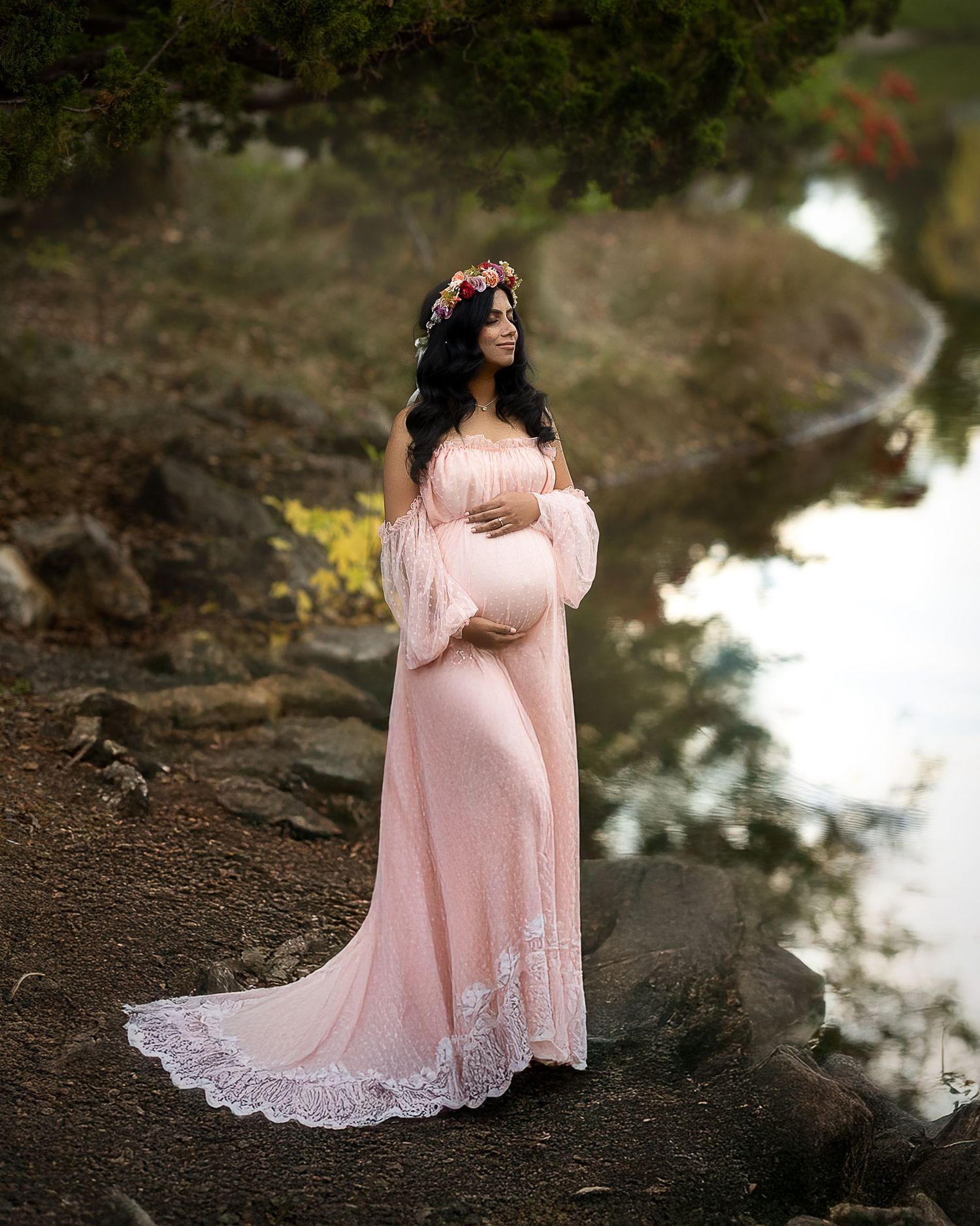 A person in a flowing pink dress stands near a reflective pond in a dreamy outdoor setting.