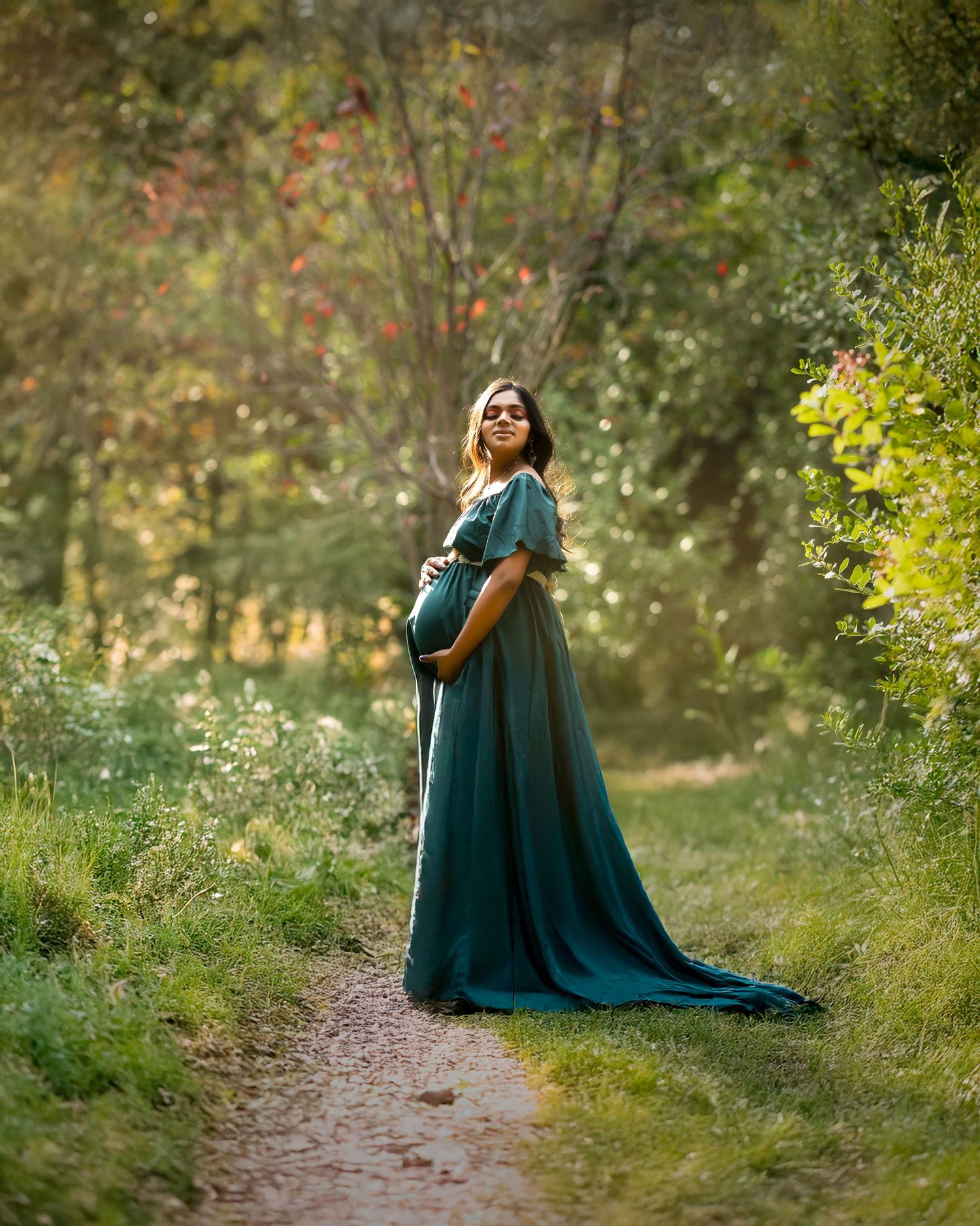A figure in a flowing teal gown walks along a wooded forest path in a dreamy autumn setting.