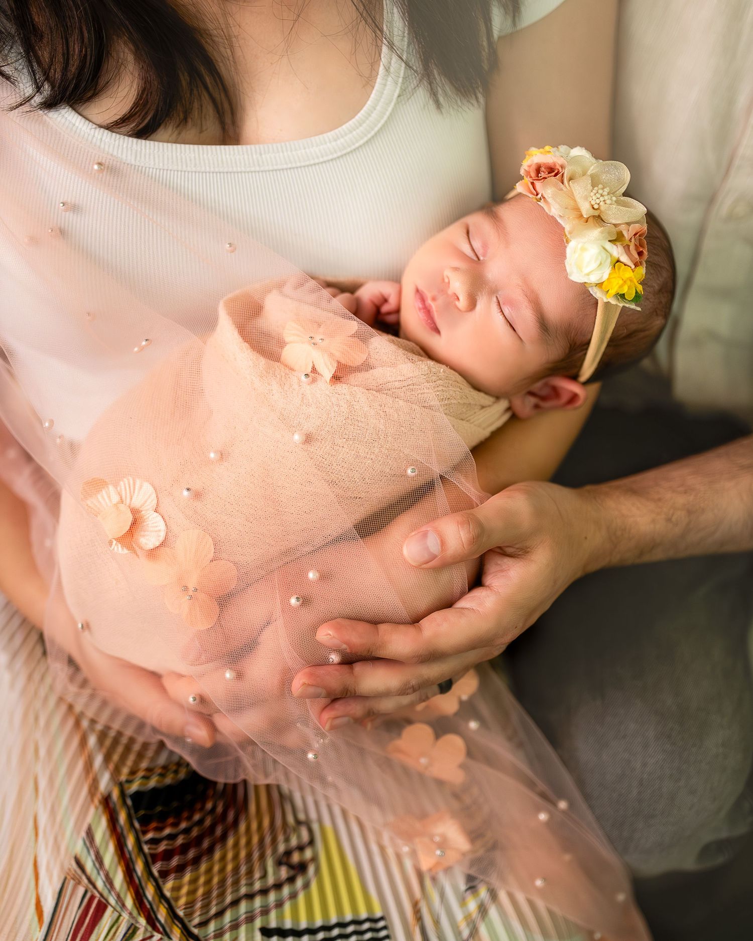 A person in a peach colored dress holds their pregnant belly while yellow flowers rest nearby.