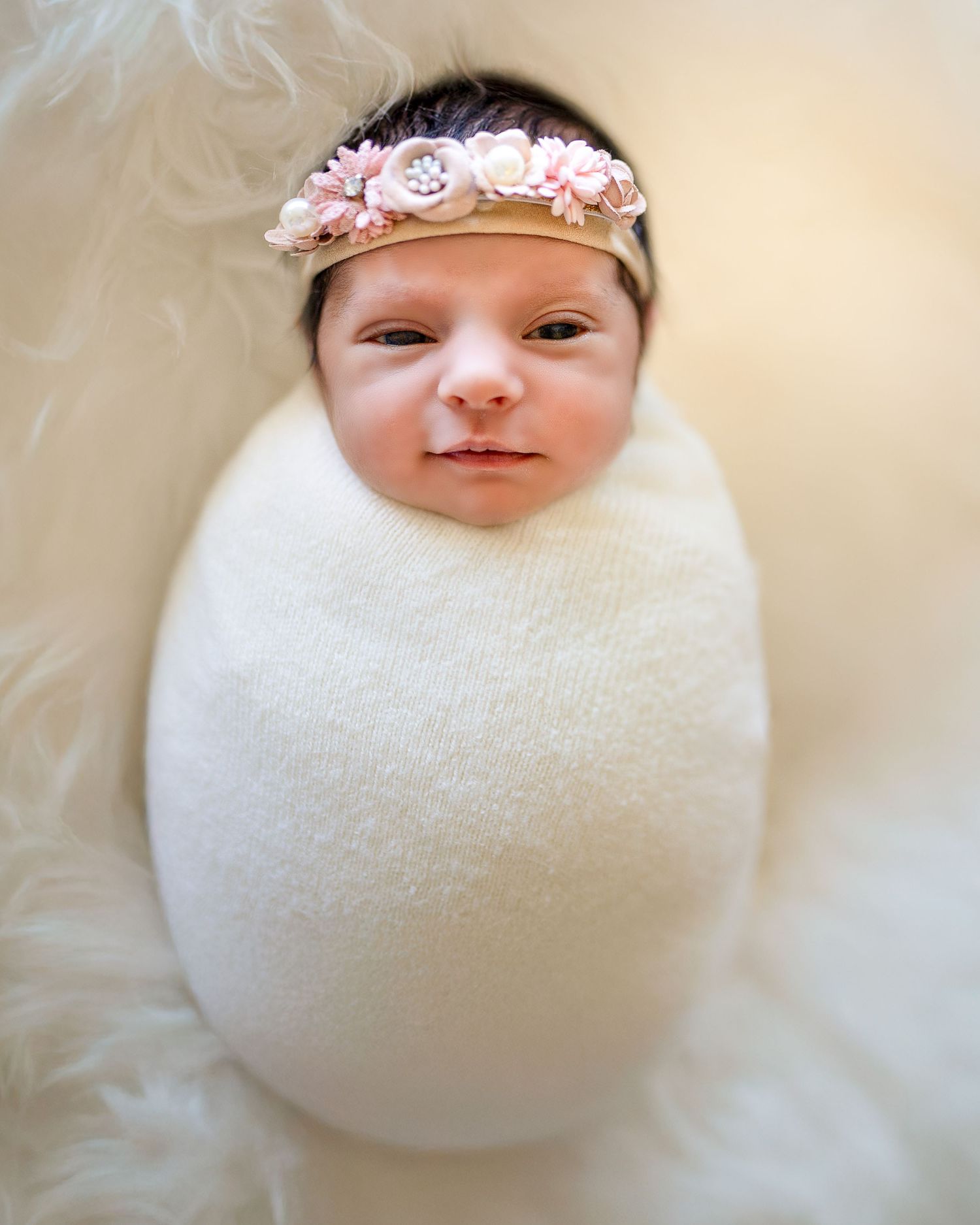 A newborn baby wrapped in white fabric wearing a delicate pink floral headband.