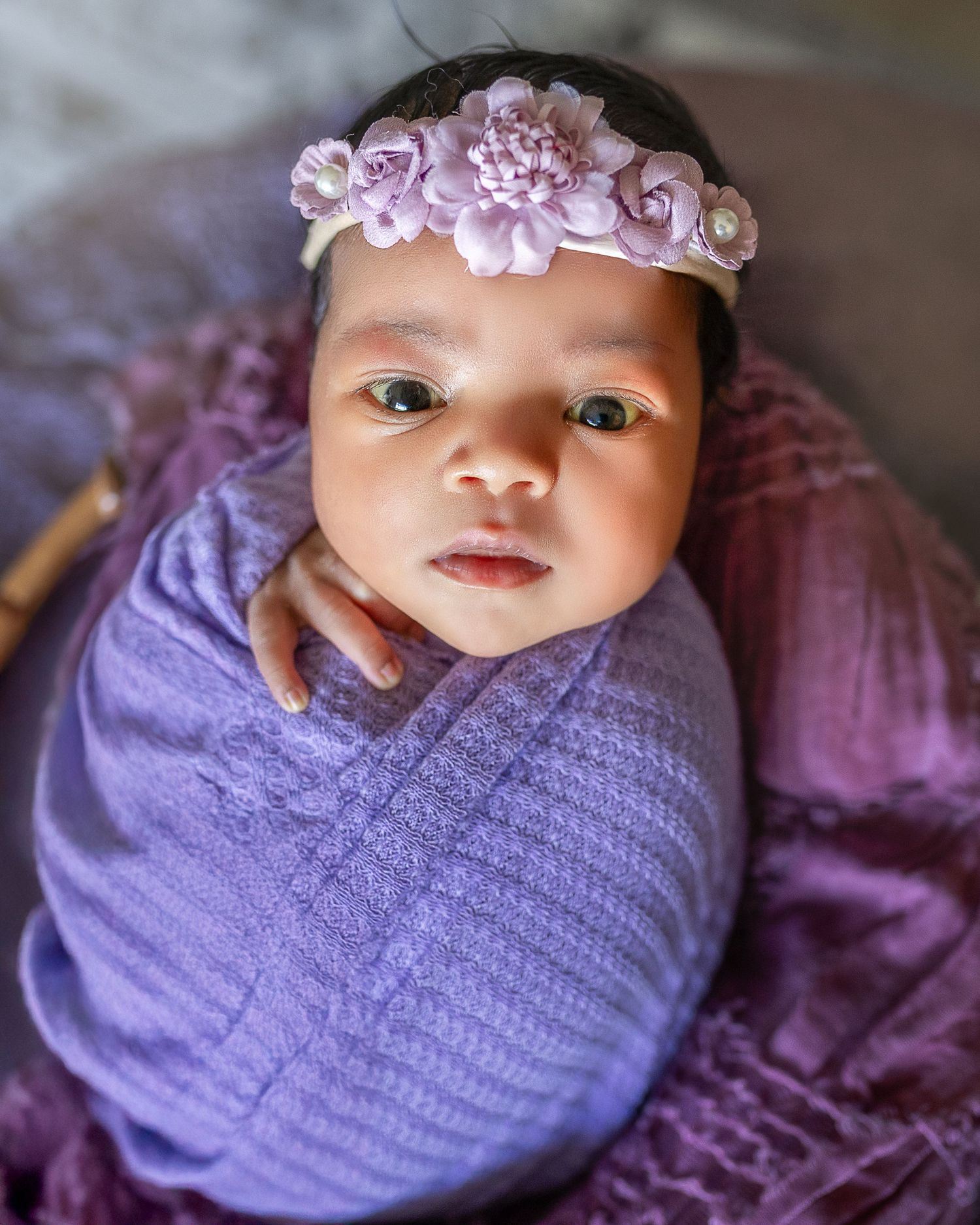 A newborn baby swaddled in purple fabric with floral decorations is photographed in a series of close-up shots.