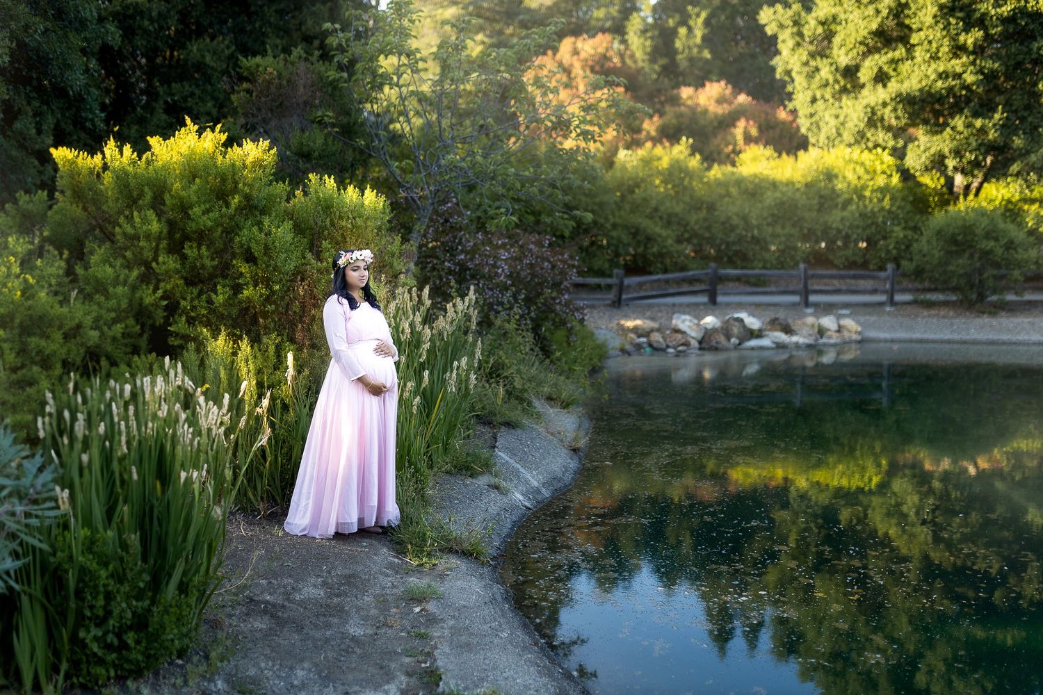 A romantic photoshoot in a lush garden setting with a pond and stone bridge during golden hour.