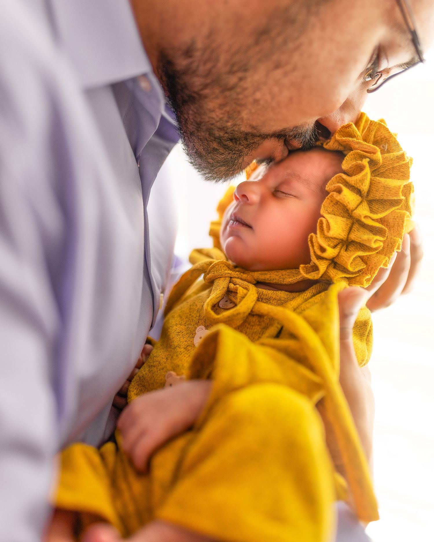 A tender moment between a sleeping baby in a mustard yellow outfit and someone leaning in close.