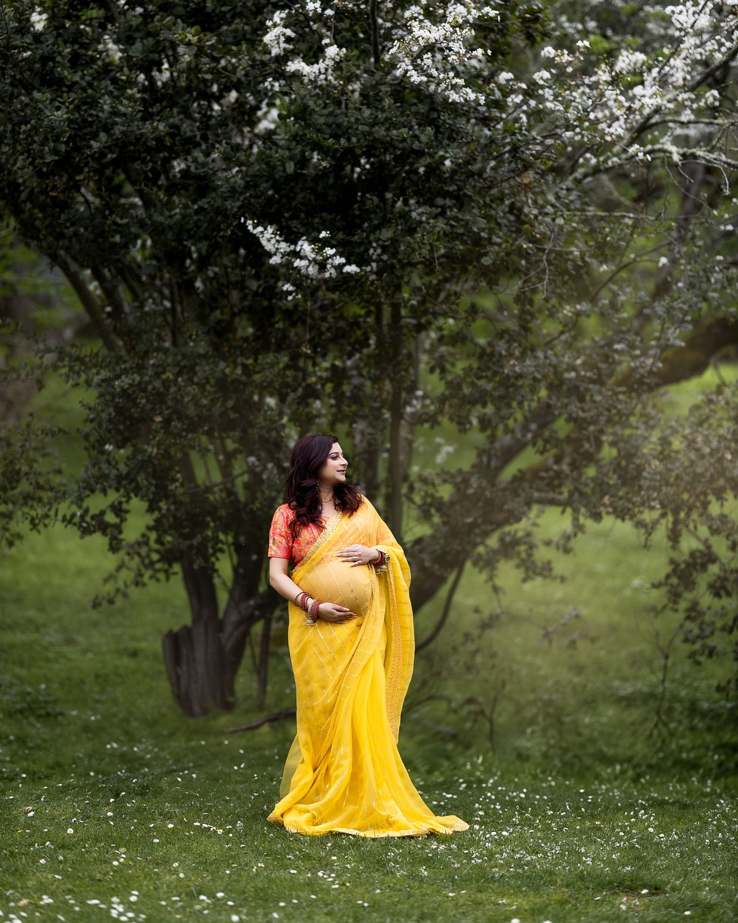 A person in a flowing yellow dress stands gracefully in a blooming spring meadow beneath flowering trees.