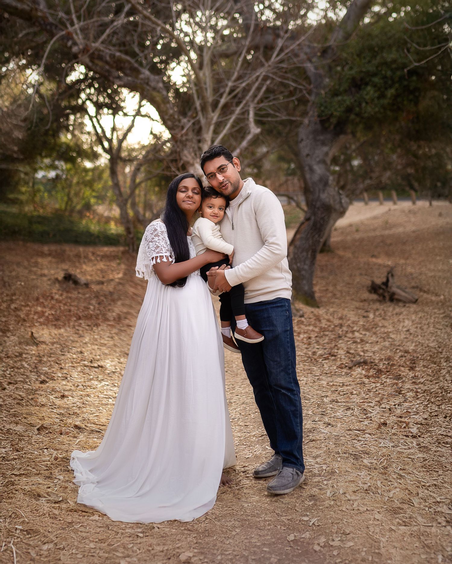 A family portrait in a rustic outdoor setting with everyone wearing white and embracing on a wooded trail.