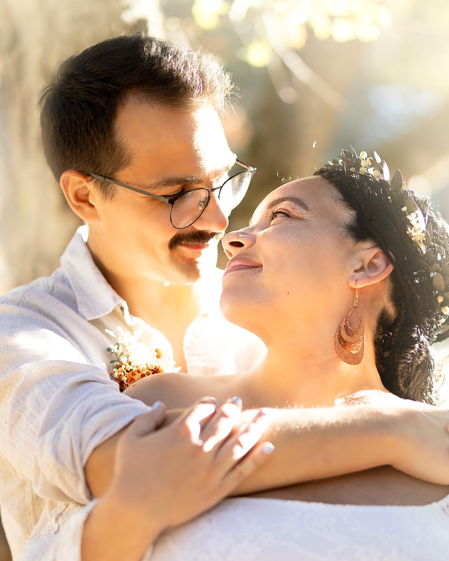 A loving couple embraces in soft sunlight, sharing an intimate moment while dressed in casual white attire.