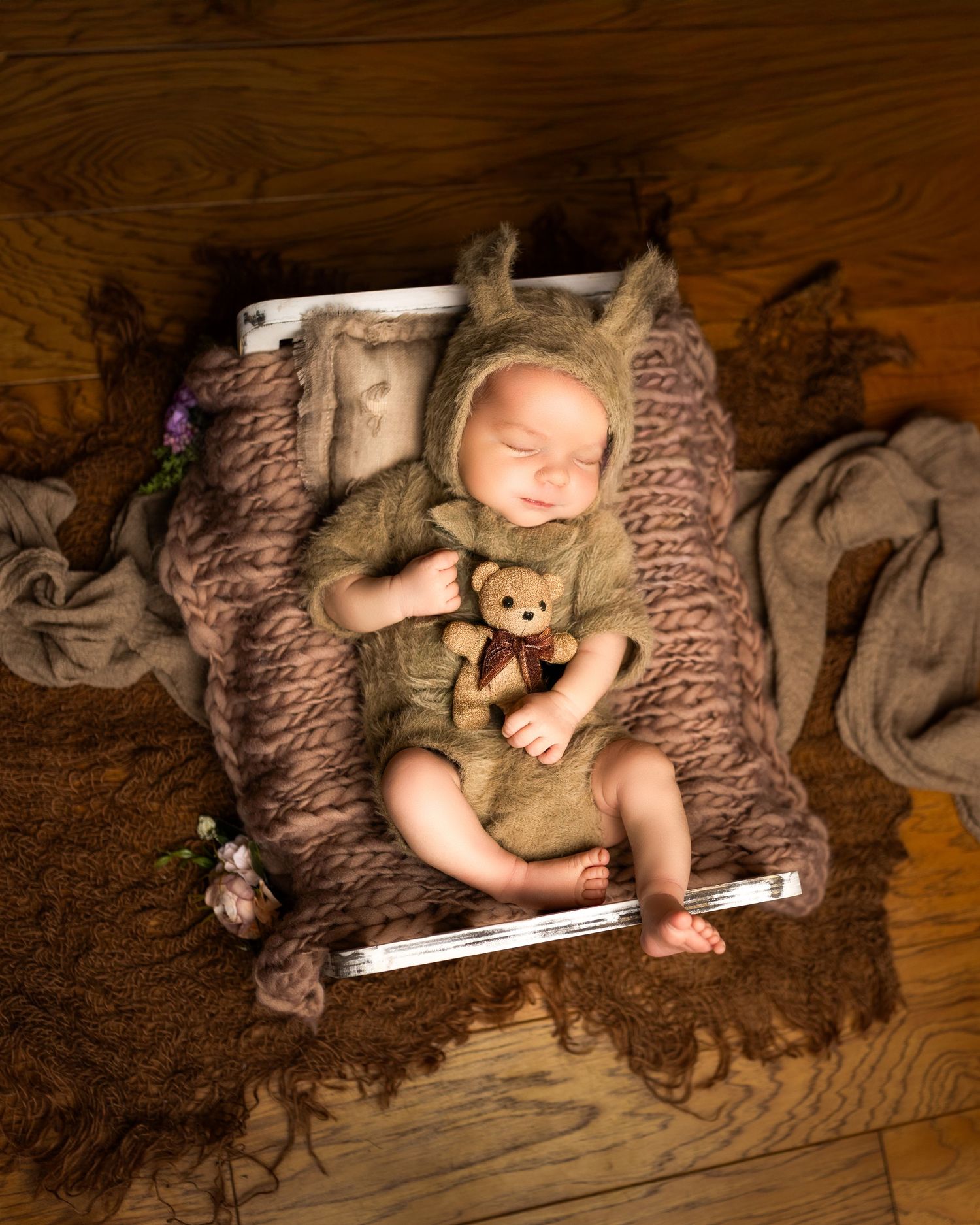 A sleeping baby lies on a brown wooden floor with a teddy bear and measuring tape in a series of progression shots.