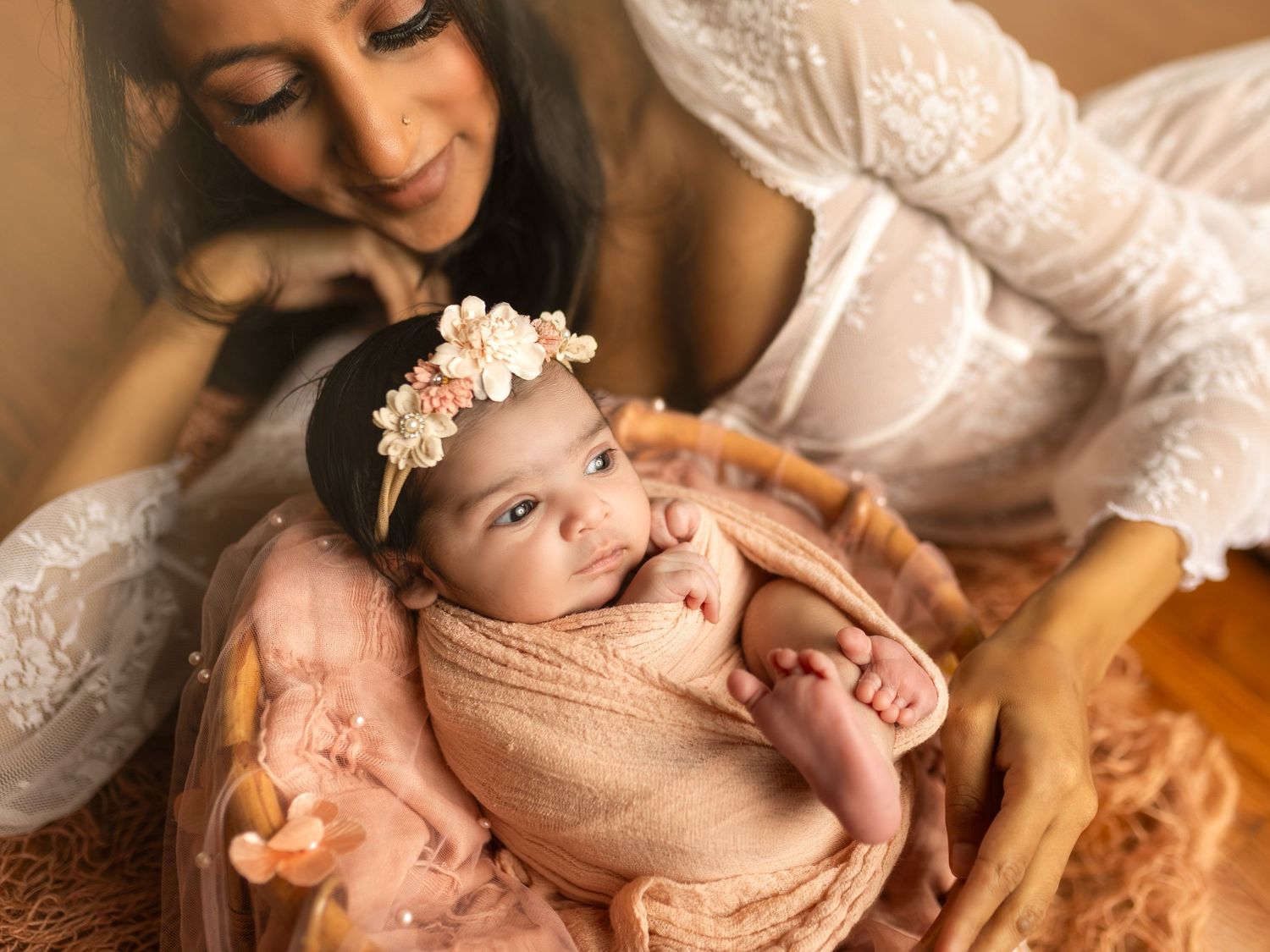 A series of tender newborn photography moments showing a baby in soft peach tones with white floral accents.