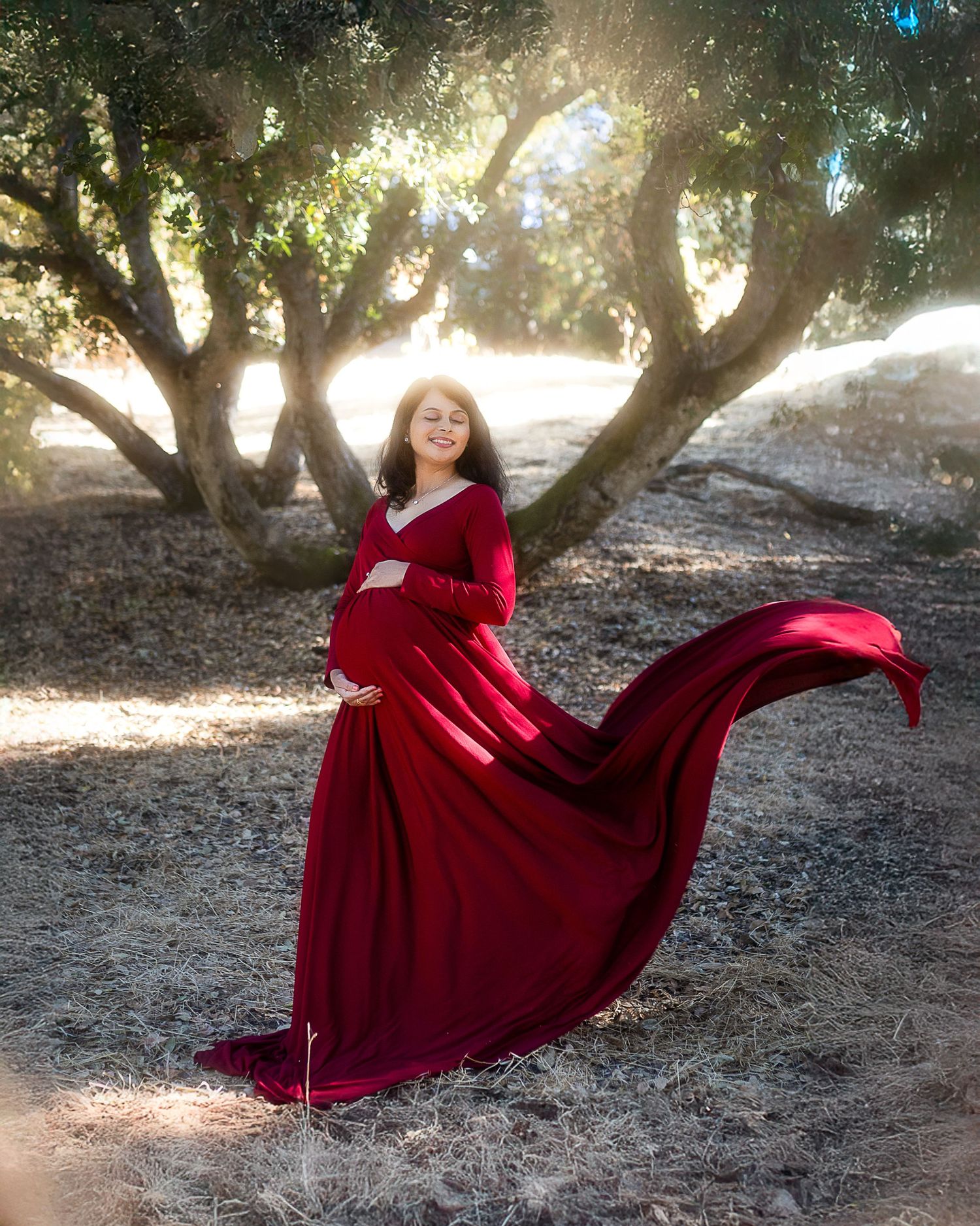 A flowing red velvet dress twirls gracefully in a sunlit forest setting, creating a romantic and ethereal atmosphere.