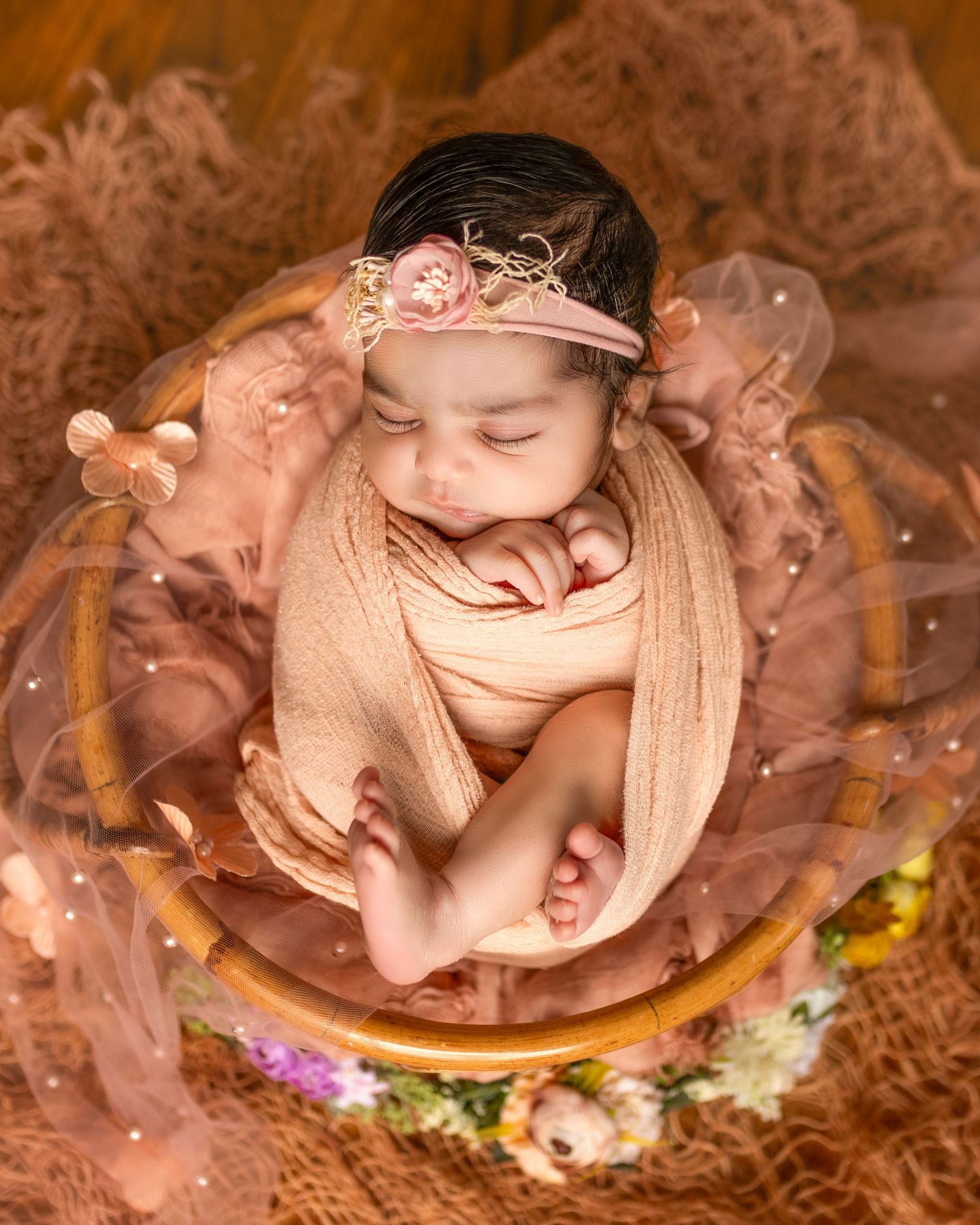 Artistic newborn photography series showing sleeping baby nestled in wooden bowl with warm brown tones and floral accents.