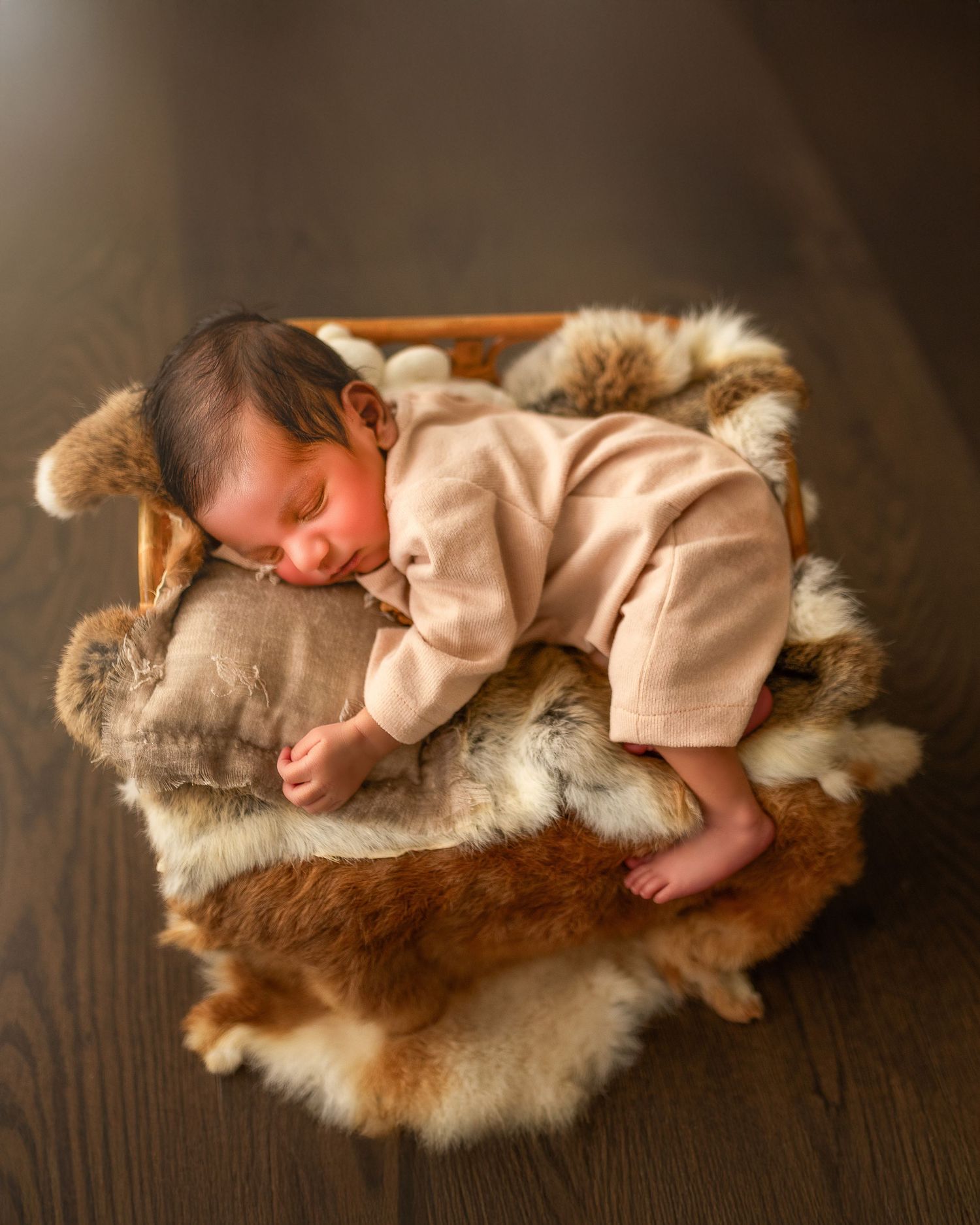 A newborn in pink clothing nestled on a soft brown fur rug during a professional photo shoot.