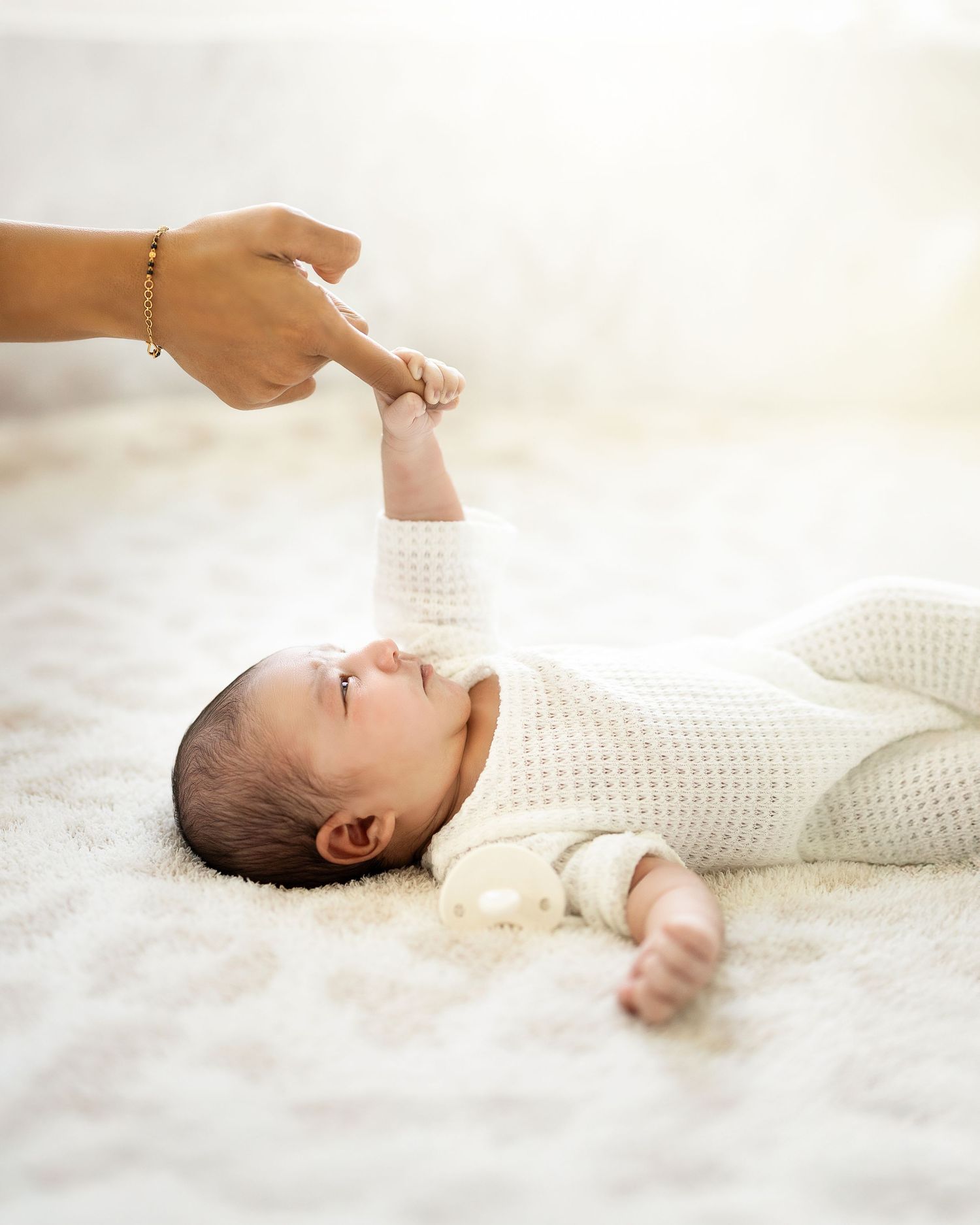 Baby in white knit sweater lying on soft white blanket during a newborn photo session.