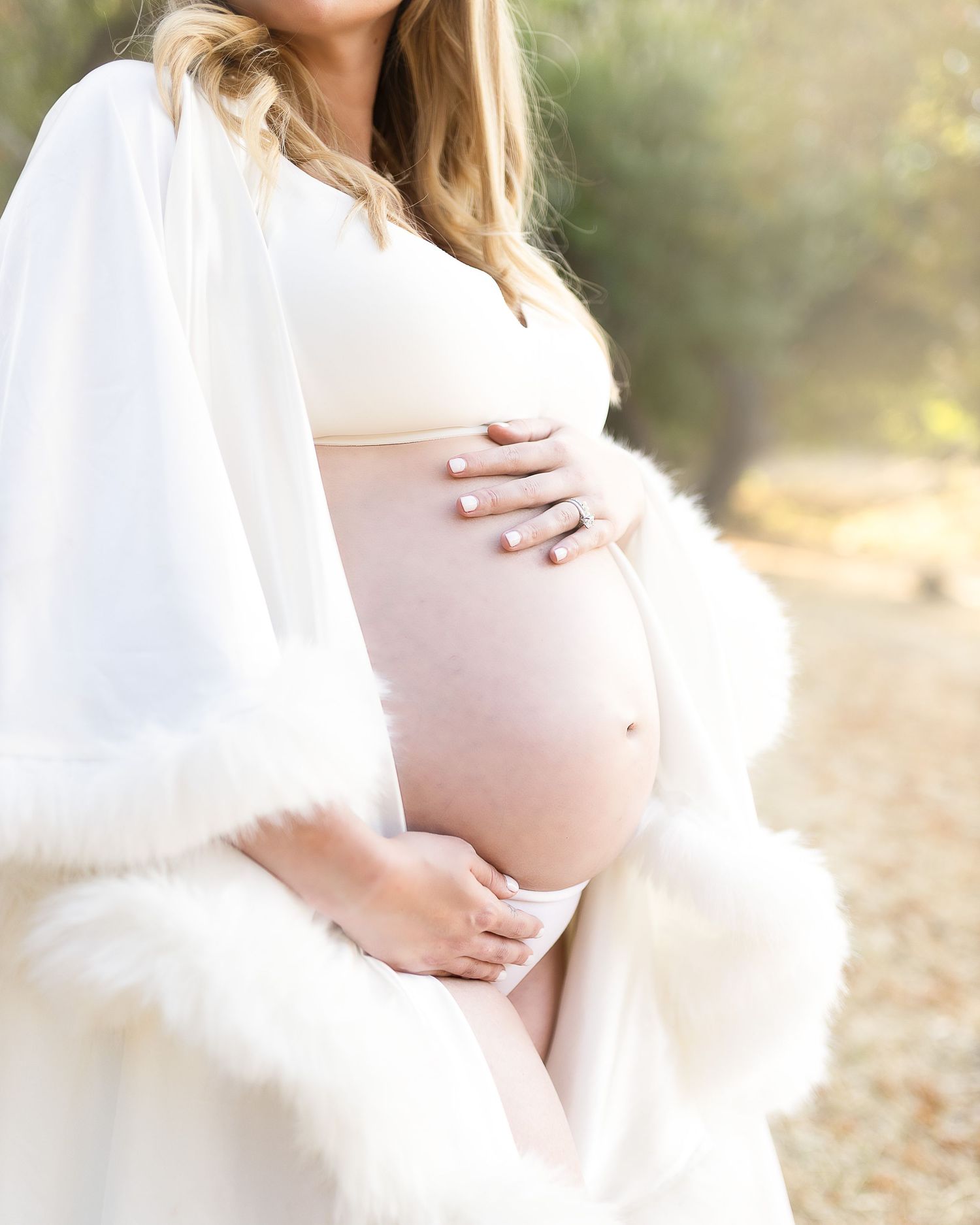 Maternity photo series showing an expecting mother in a white dress cradling her belly in soft natural lighting.