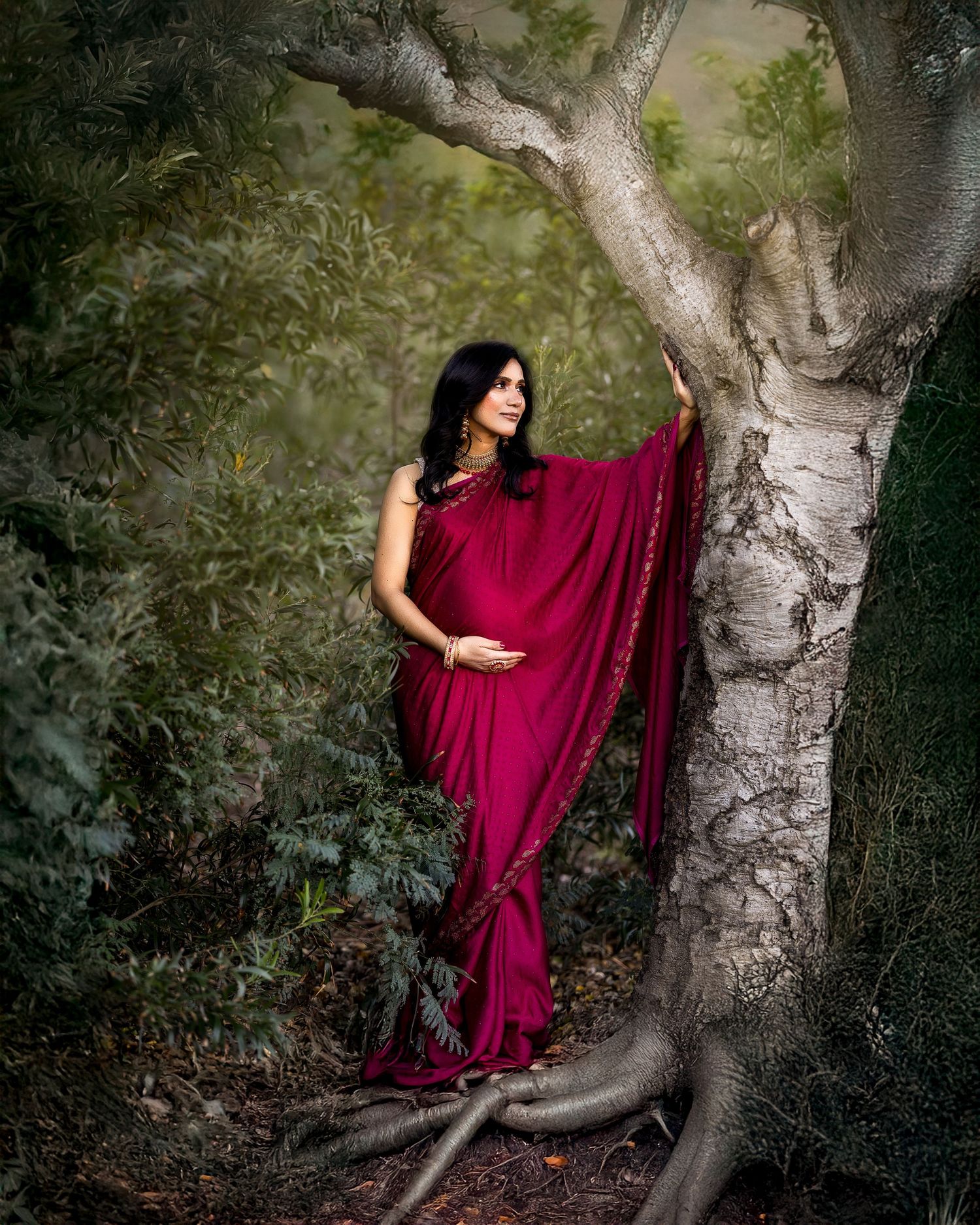 Dramatic forest photoshoot featuring burgundy dress against textured tree bark in dappled sunlight.