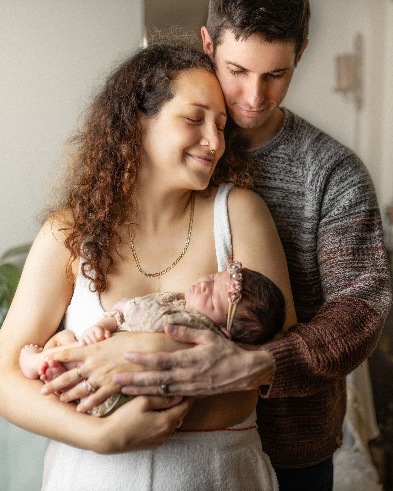 New parents in cozy home smiling down at their sleeping newborn baby together.