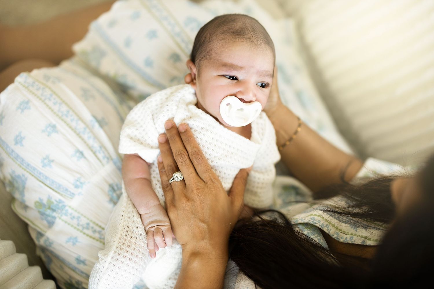 A series of photos showing a baby lying on white bedding while wearing a diaper and smiling.