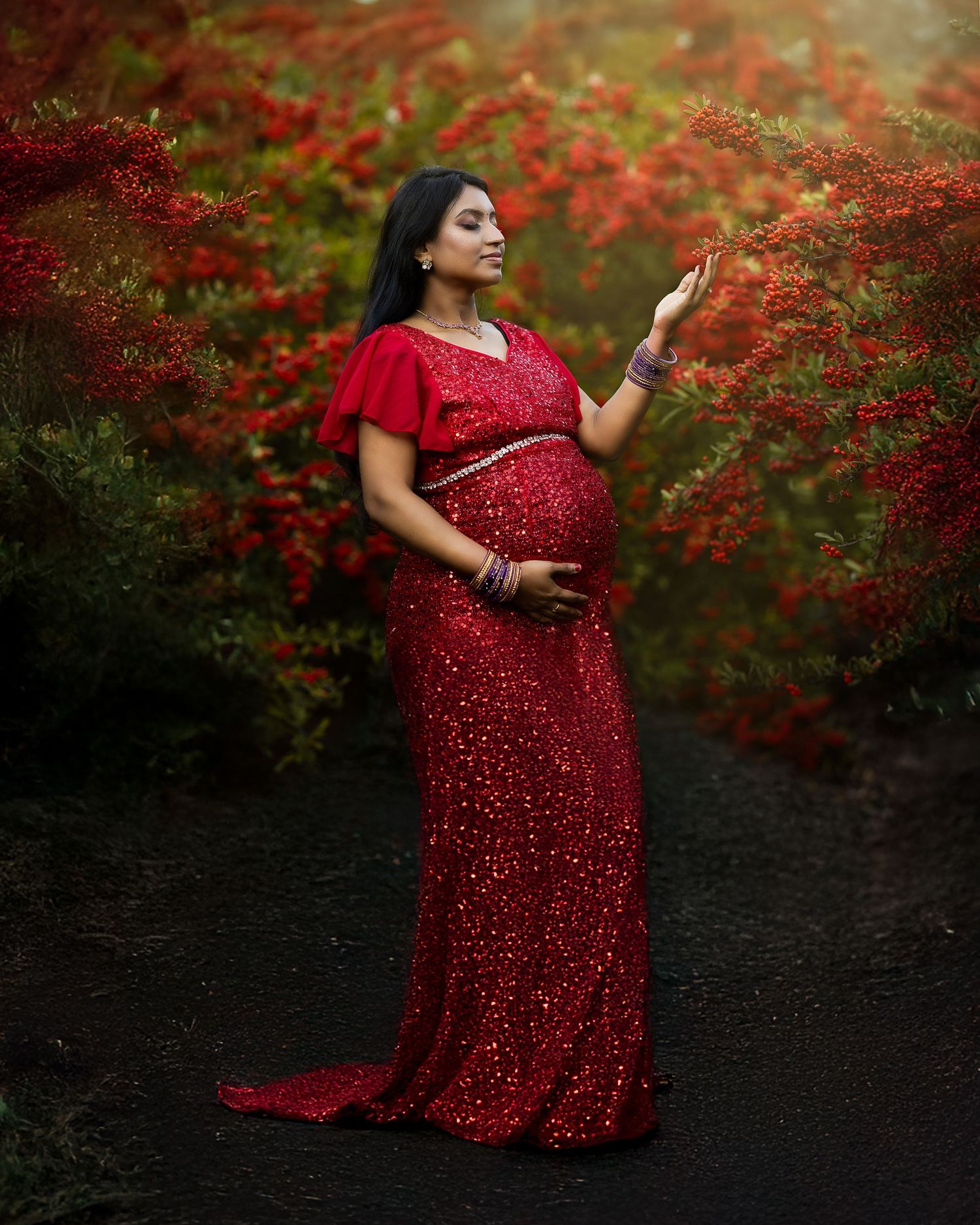 A maternity photoshoot featuring a woman in a sparkly red dress against vibrant autumn foliage.