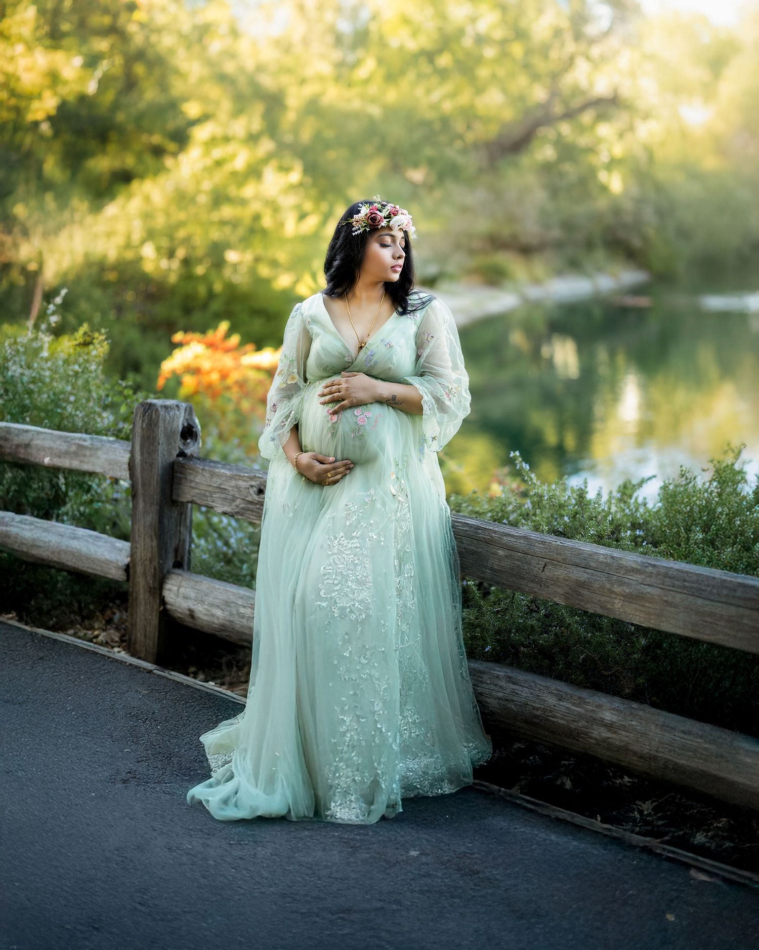 A person in a mint green lace gown poses gracefully by a wooden fence during golden hour in a garden setting.