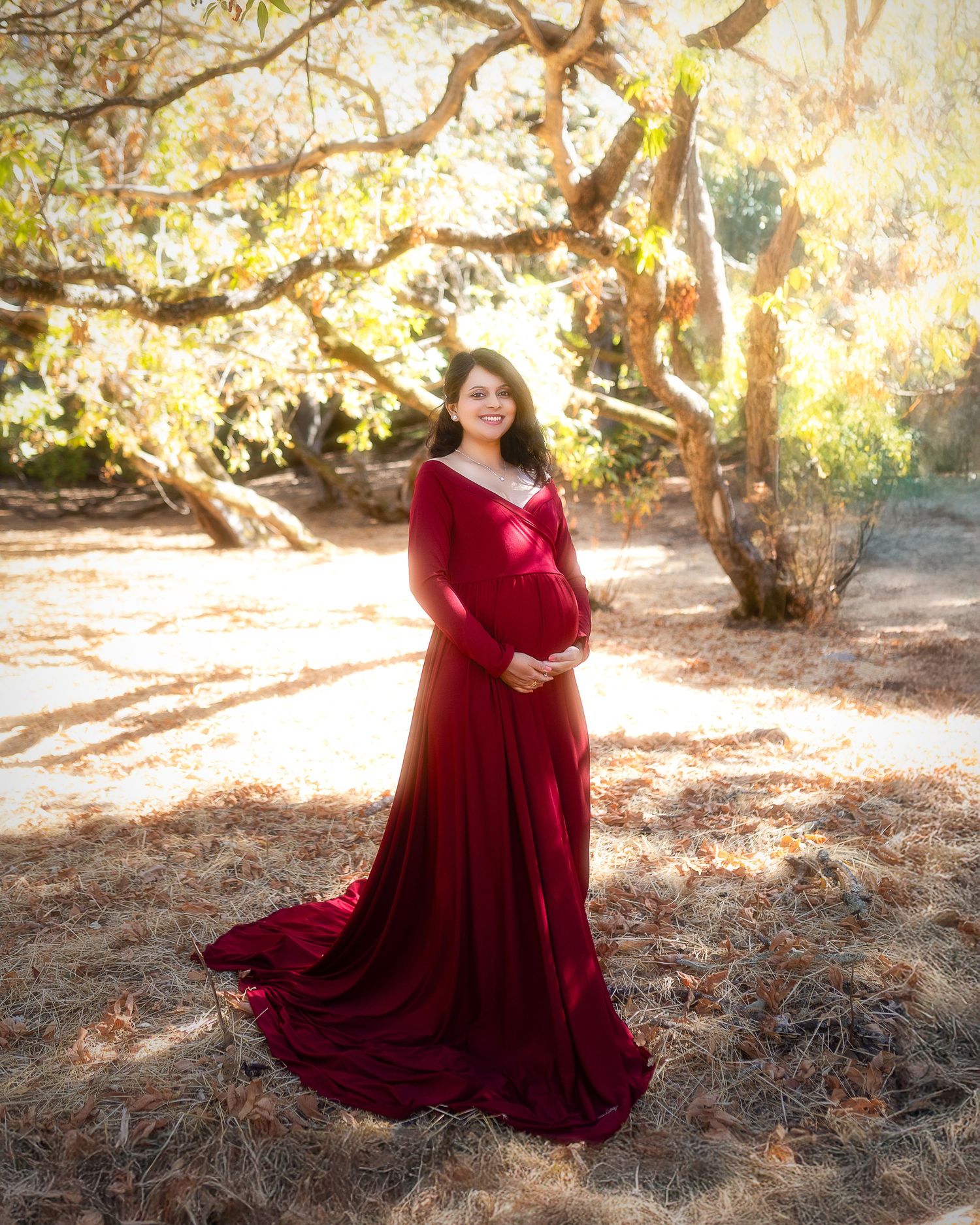 A flowing burgundy velvet dress twirls gracefully in a sunlit forest setting during a golden hour photoshoot.