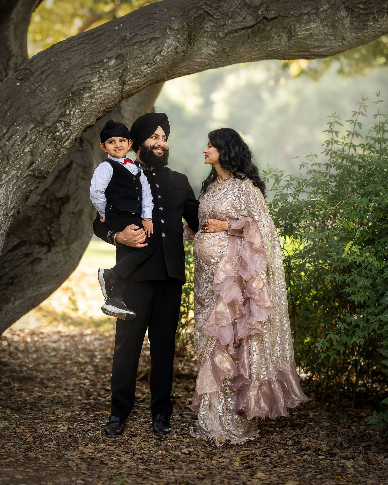 A couple shares intimate moments under a large tree branch in formal attire during an outdoor photo session.