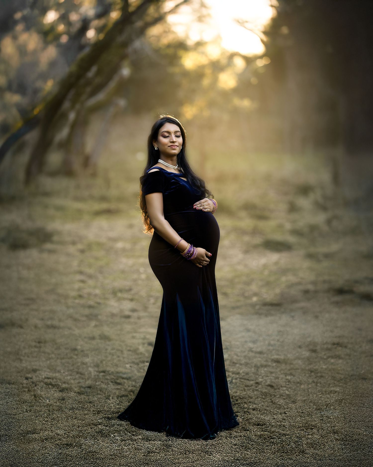 A figure in a flowing black dress stands in a misty forest setting during golden hour.