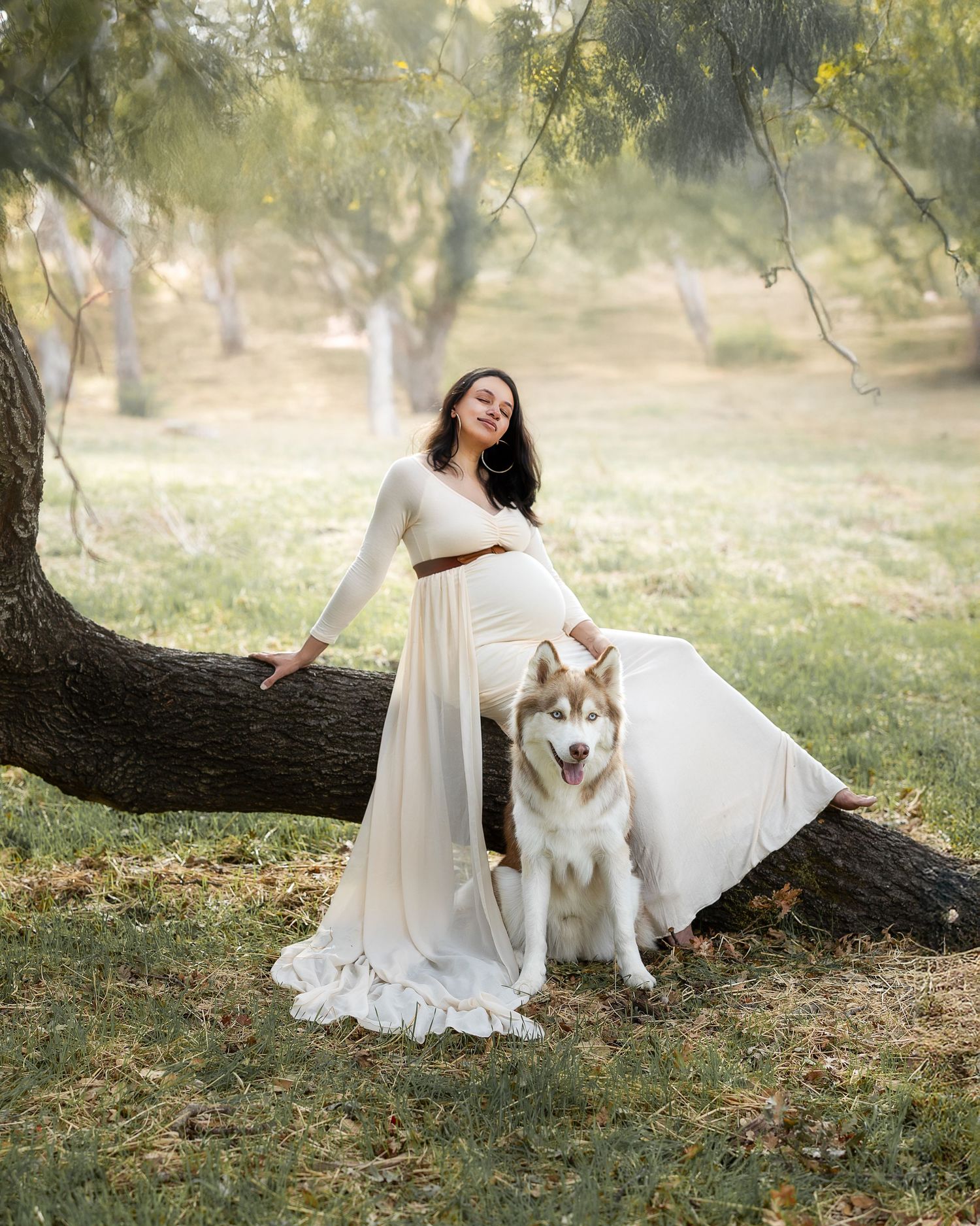 A beautiful white dress flows in an outdoor setting with a majestic Husky dog sitting beside a tree.
