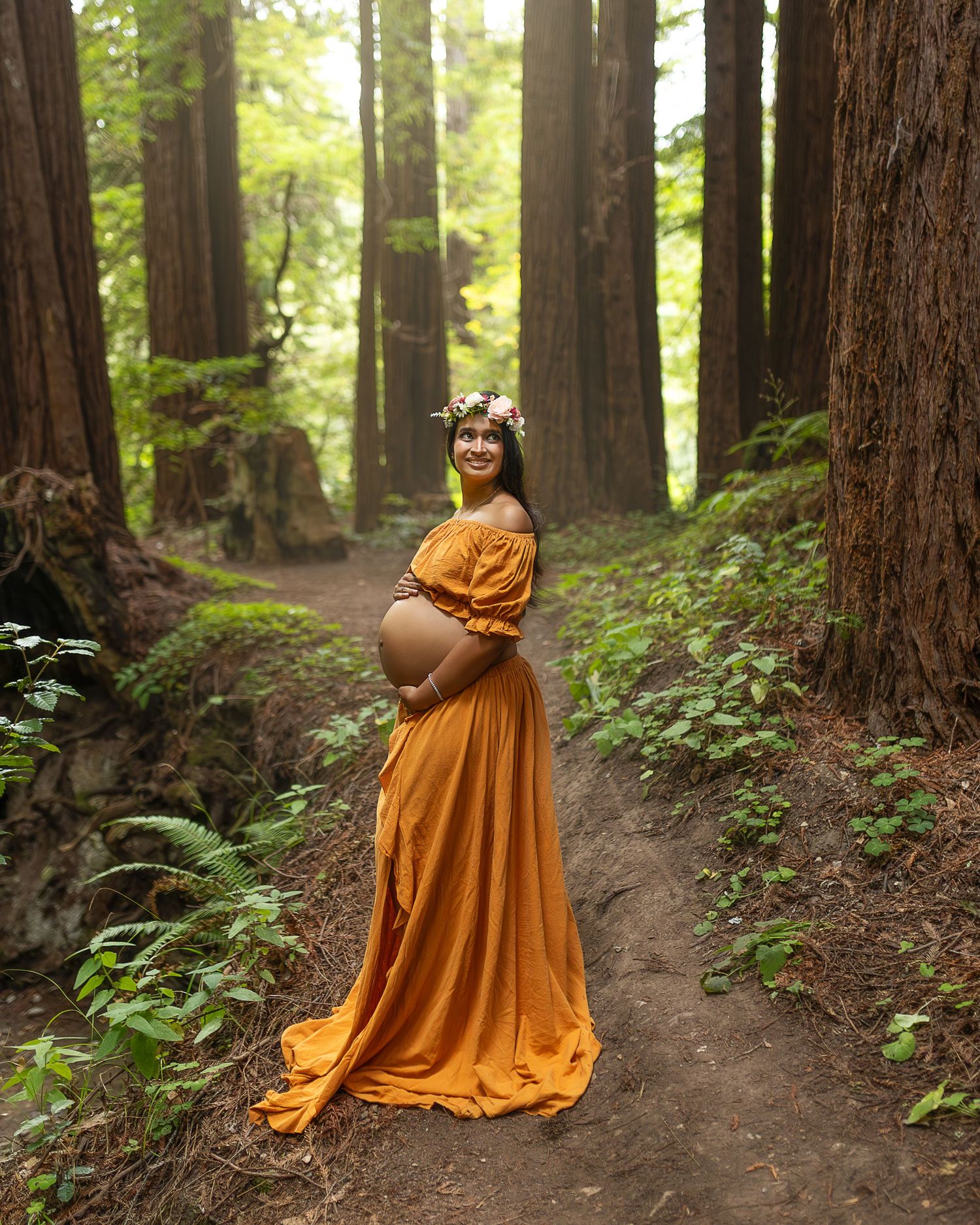 A flowing orange dress twirls through a mystical redwood forest path in dramatic motion.