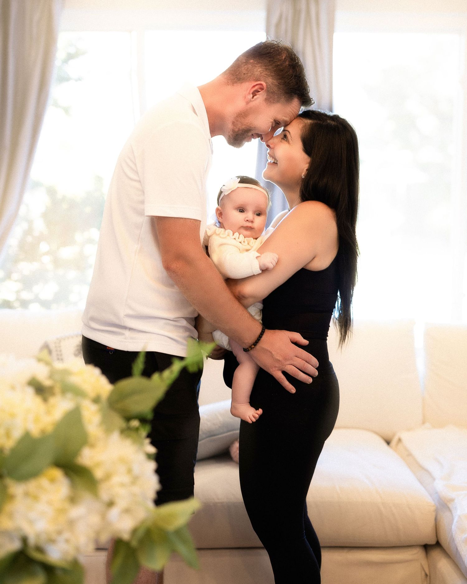 A couple in a bright living room sharing a tender moment while holding their adorable baby dressed in blue.