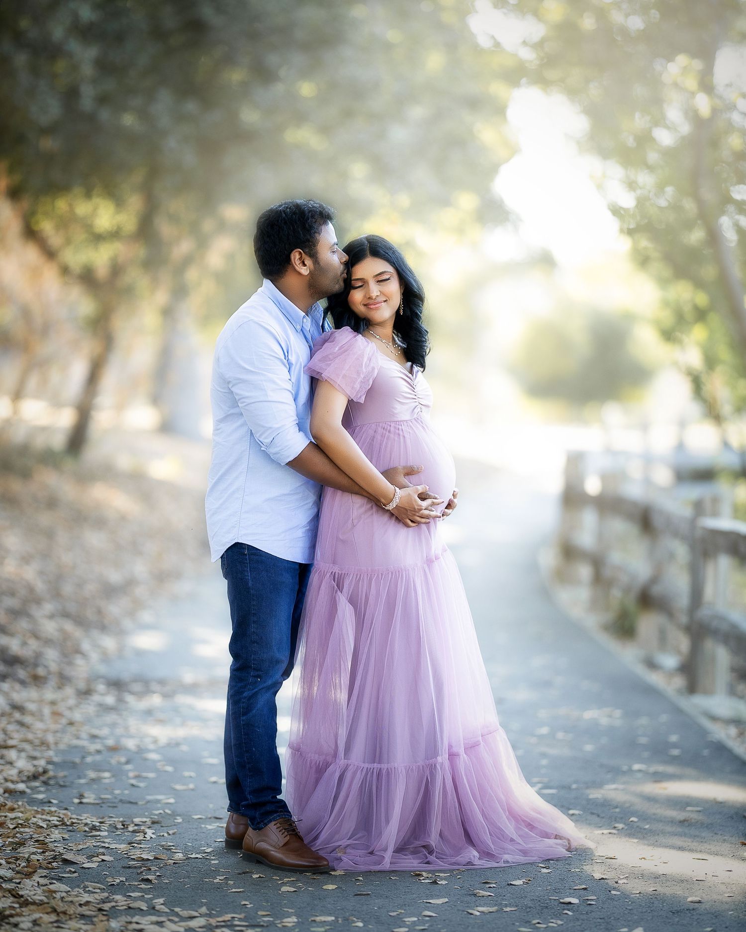 A romantic couple poses together outdoors in a dreamy setting with the person in a flowing pink tulle gown.
