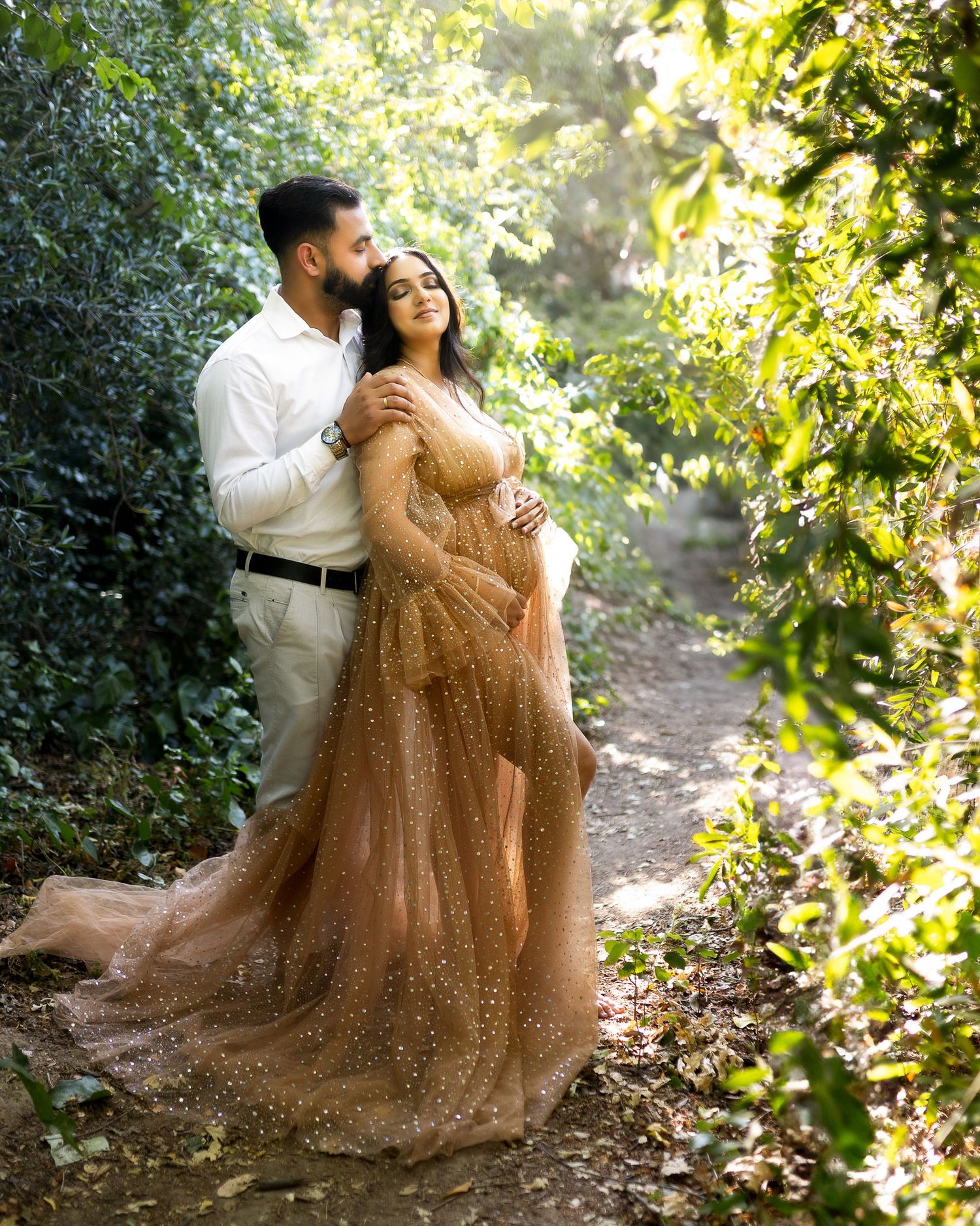 A couple in romantic poses along a sunlit garden path, with the person in a sparkly brown gown creating ethereal moments.