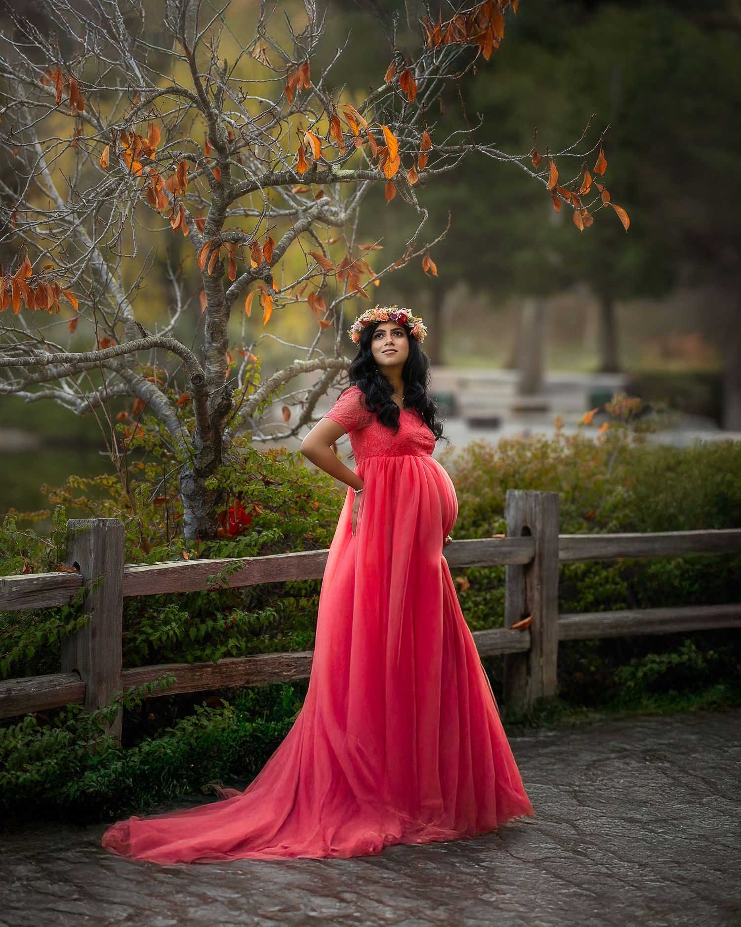 A flowing red tulle gown creates a dramatic silhouette against an autumn garden backdrop with a rustic wooden fence.