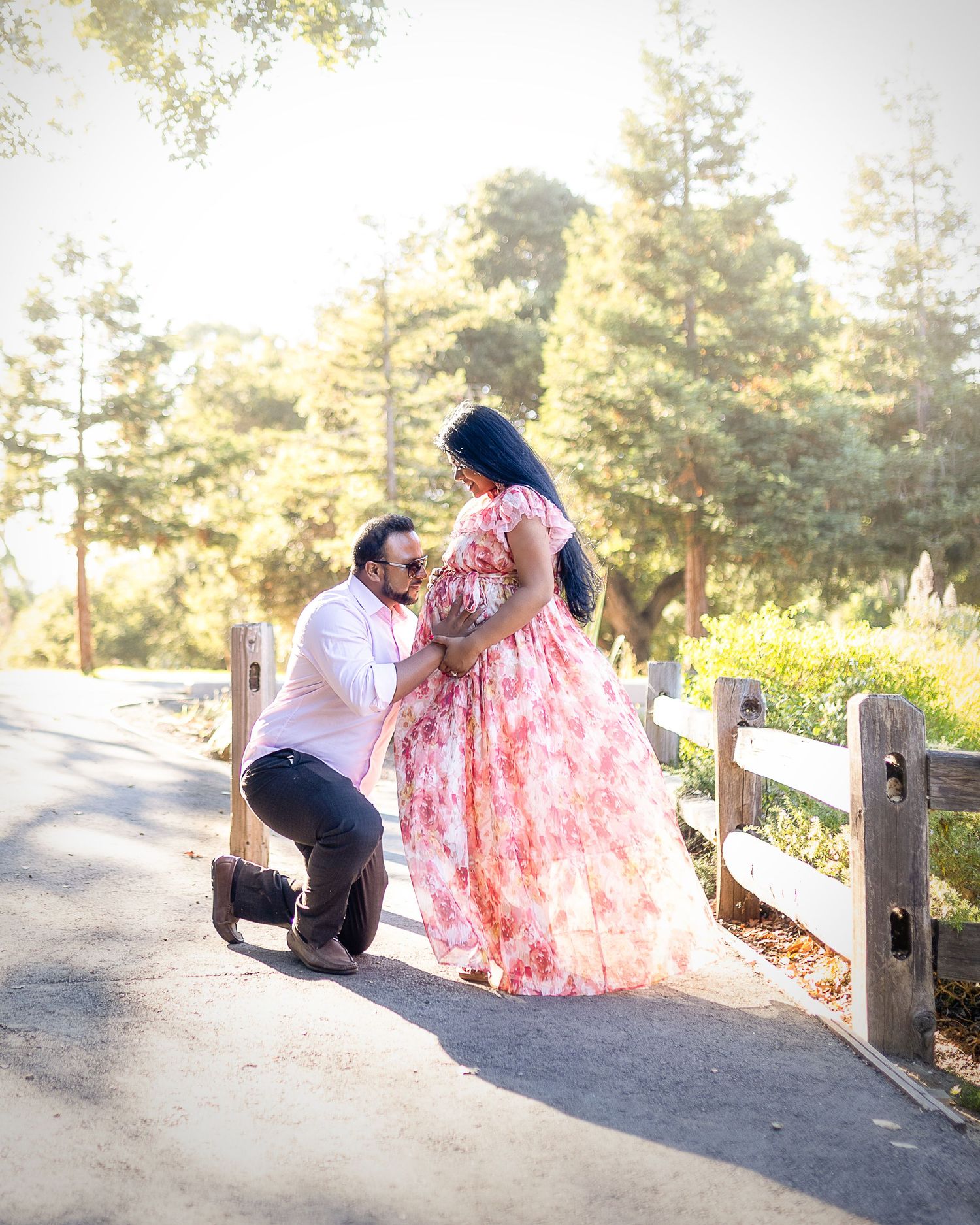 A couple shares a romantic moment on a rustic wooden fence overlooking a scenic mountain landscape at sunset.
