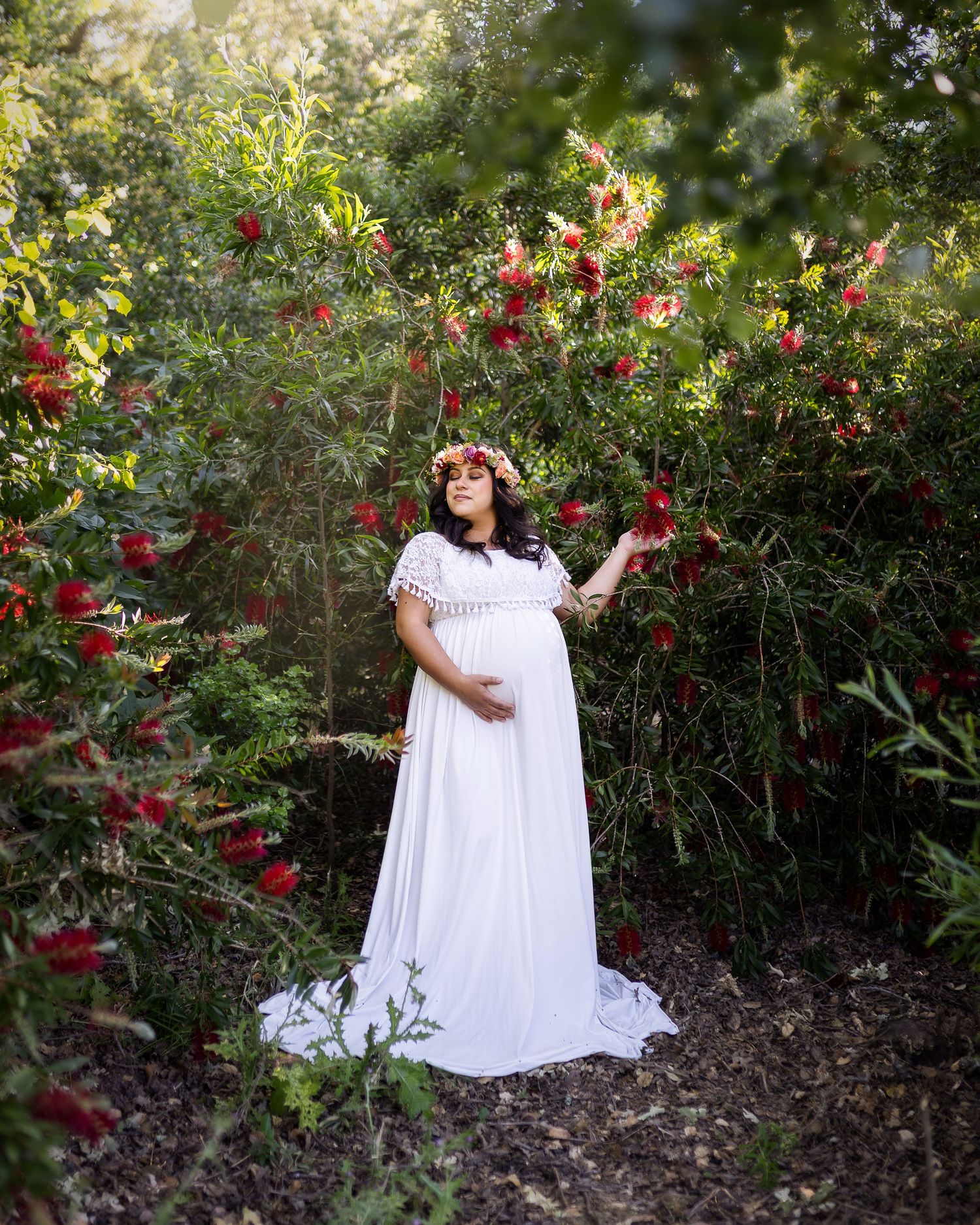 A dreamy garden scene with red roses surrounds a figure in a flowing white dress and floral crown standing among the blooms.