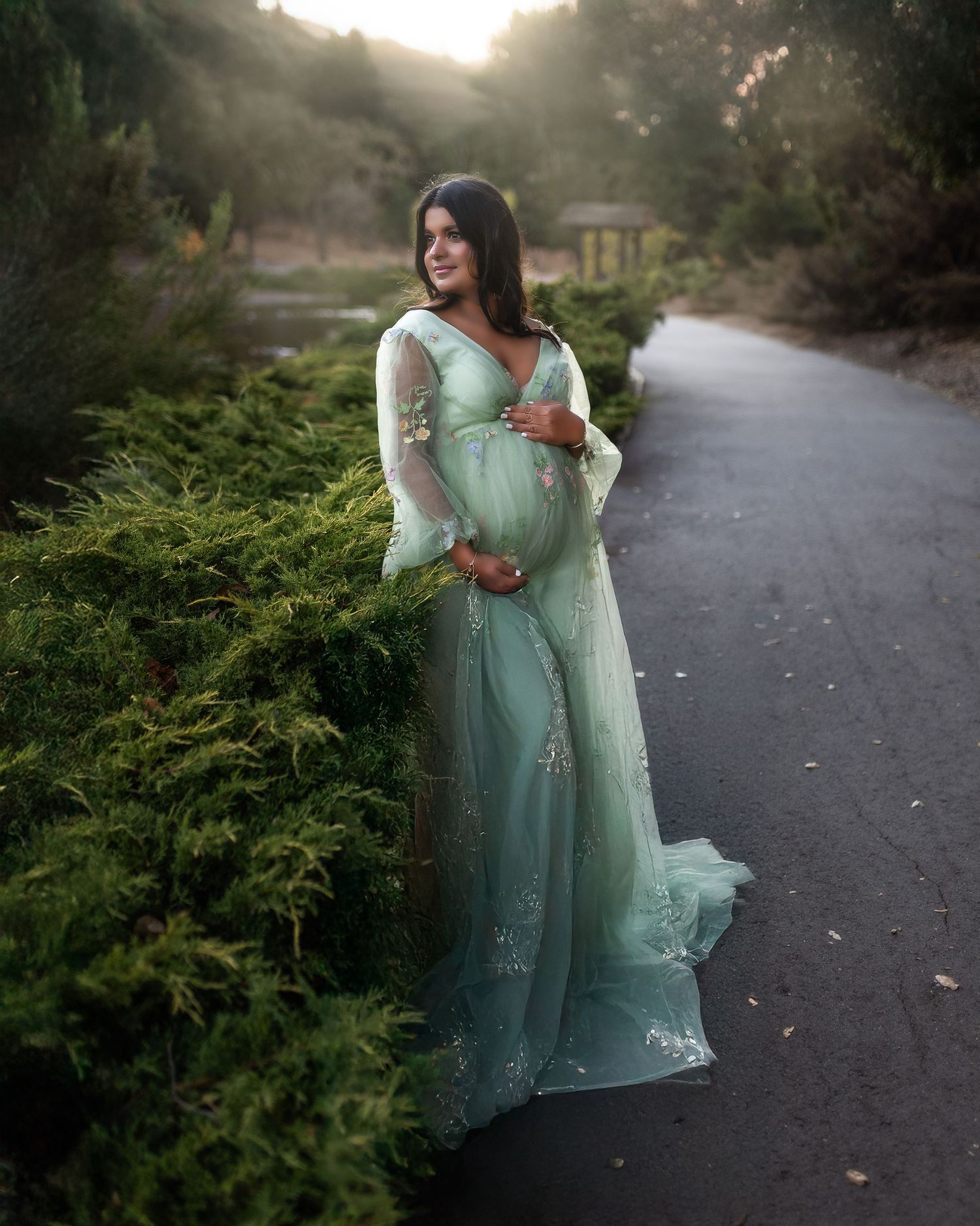A person in a flowing mint green dress poses on a winding path during golden hour at sunset.