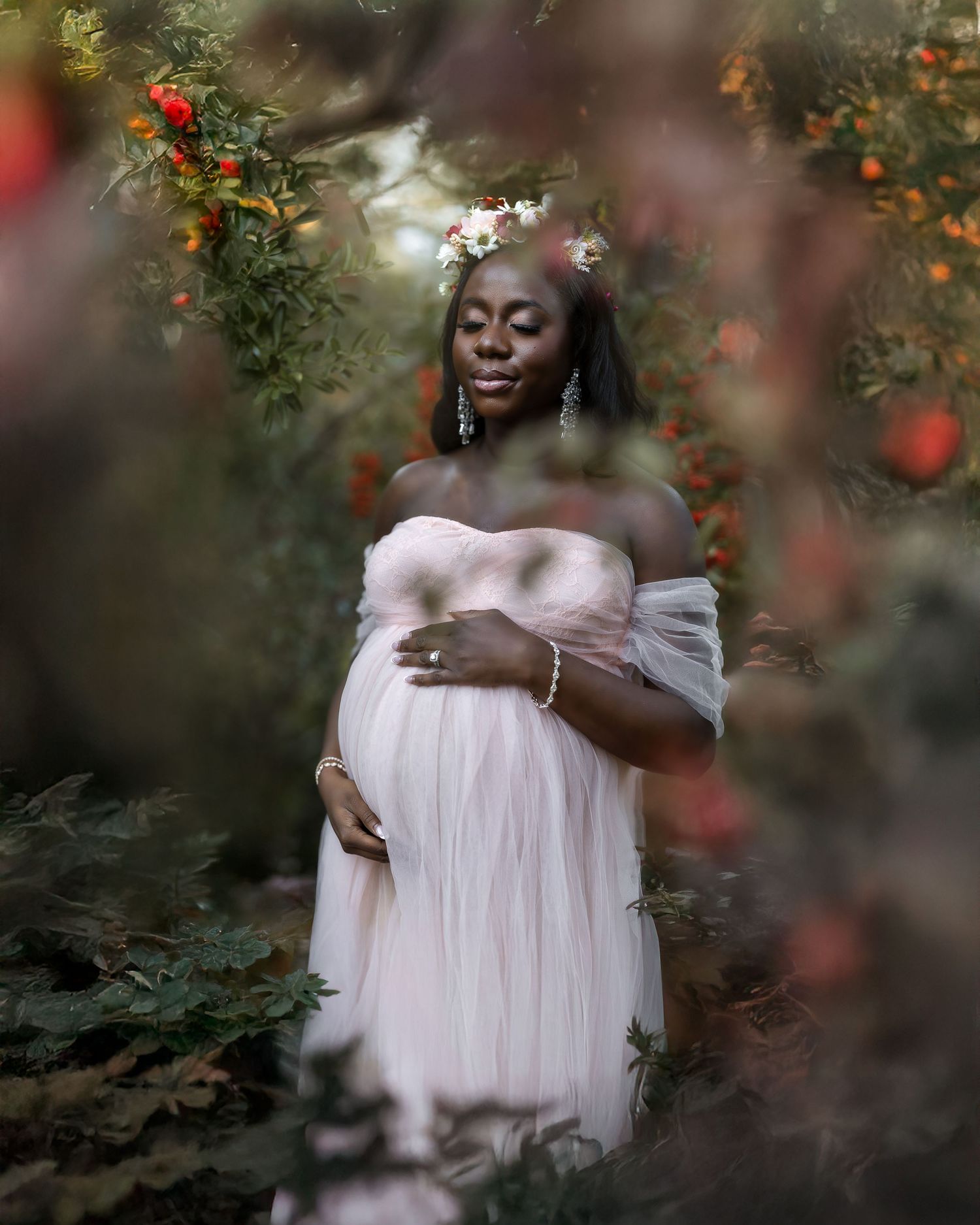 Dreamy maternity portrait session with soft pink dress framed by delicate red berries and natural foliage.