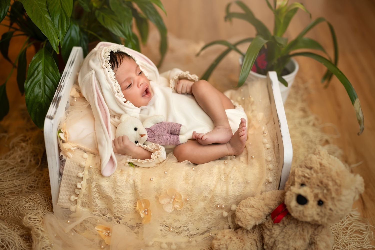 A sleeping baby rests on a cream-colored blanket in a vintage-inspired photography setup with soft lighting.