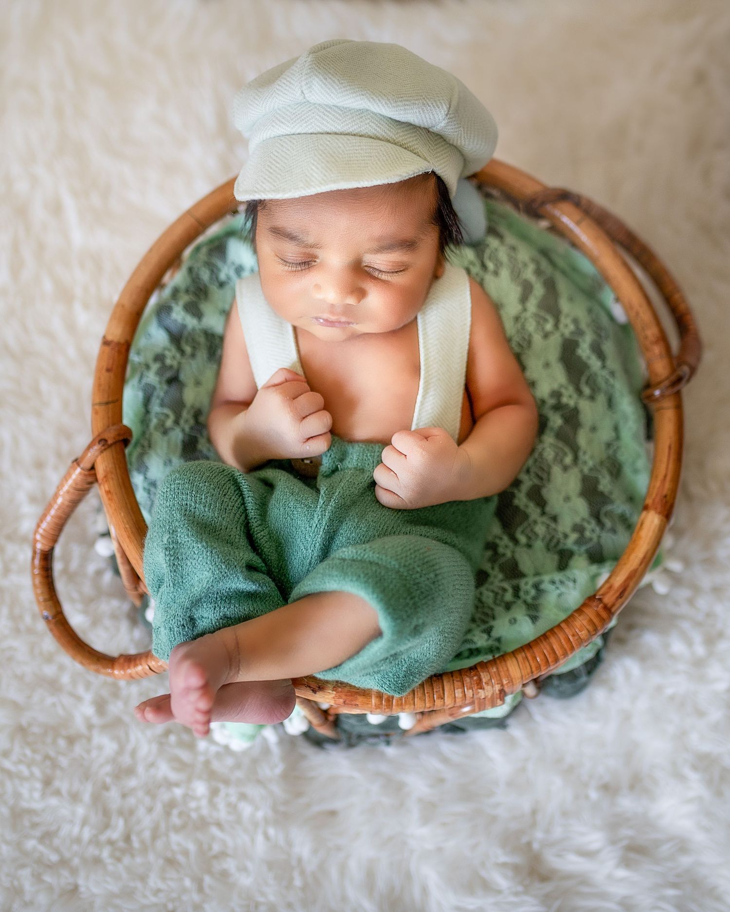 Sleeping newborn baby wrapped in green blanket lying in curved wooden basket on textured beige background.