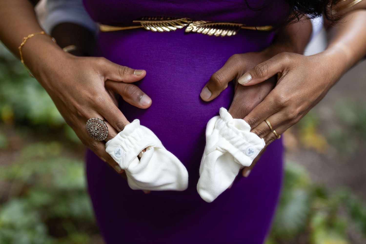 Close-up view of hands holding white wedding shoes against a purple dress background.