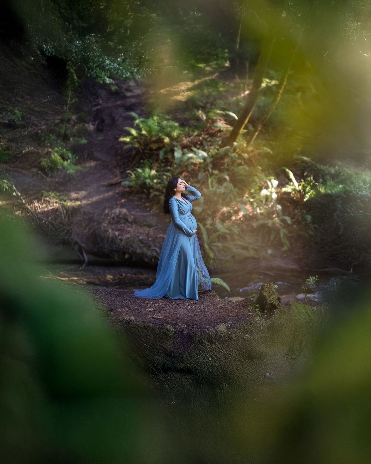 A figure in a medieval-style blue gown sits contemplatively among trees in a mystical woodland scene.