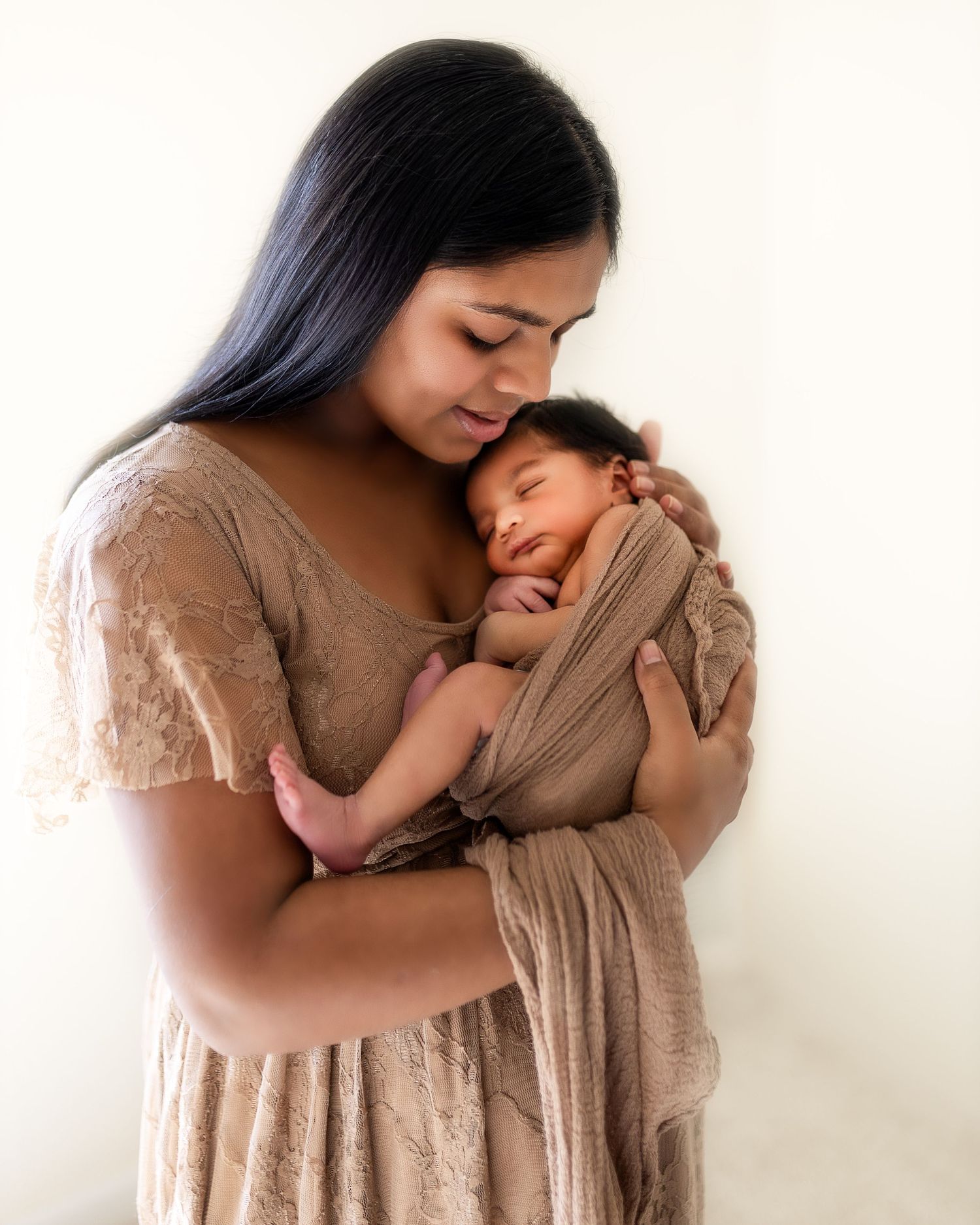 A tender moment between mother and newborn baby in neutral tones shows gentle nurturing and bonding.