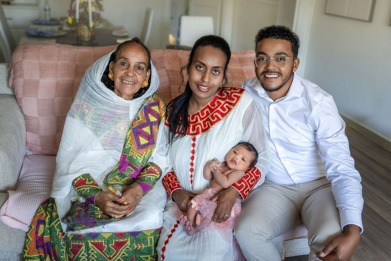 Family members in white and colorful outfits sitting together on a couch during a casual photo session.