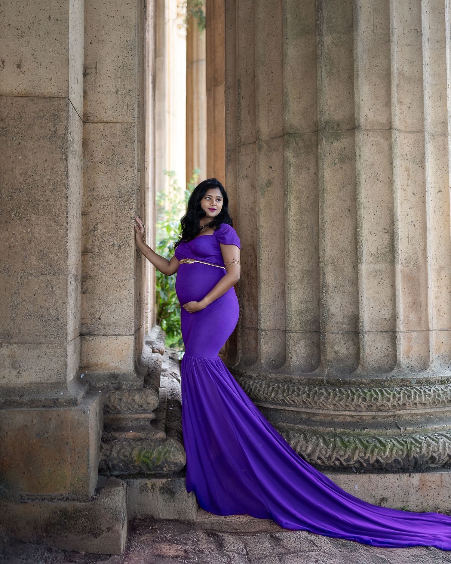 A person in a flowing purple gown poses dramatically between stone columns in a classical architectural setting.
