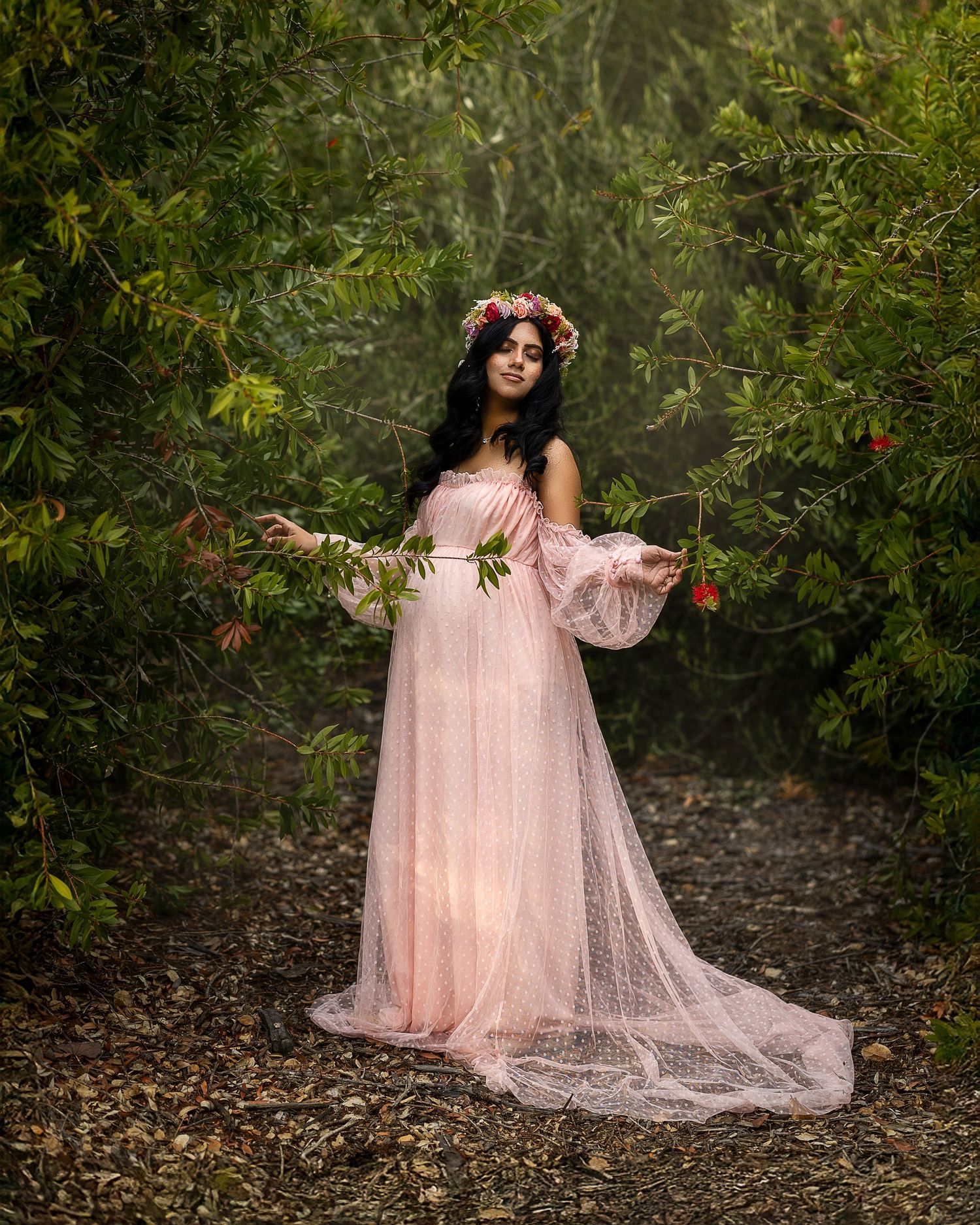 A romantic scene in a wooded area features a flowing pink tulle dress against lush greenery and natural light.